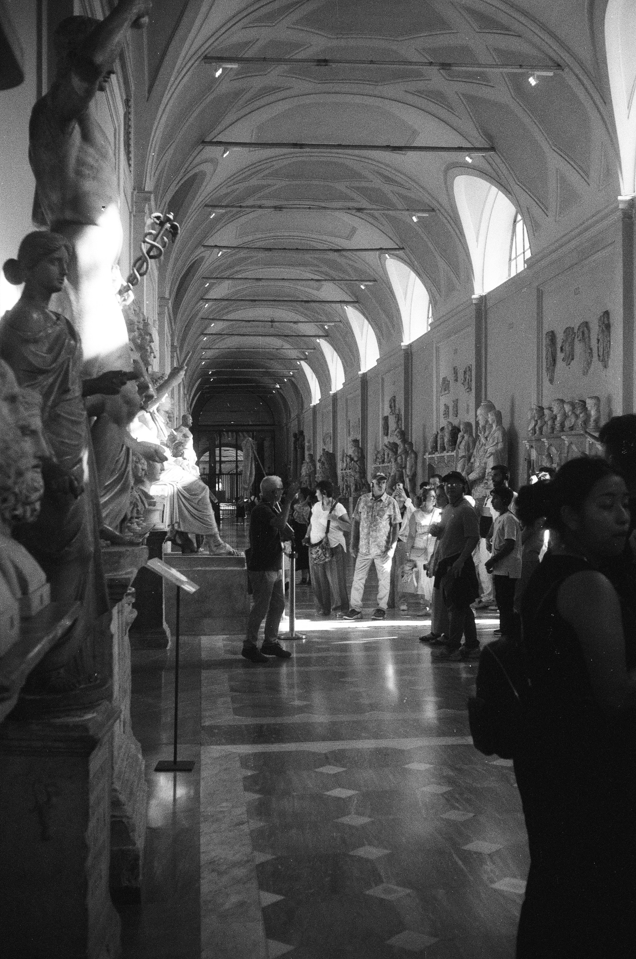 People walking through a long art gallery with sculptures.
