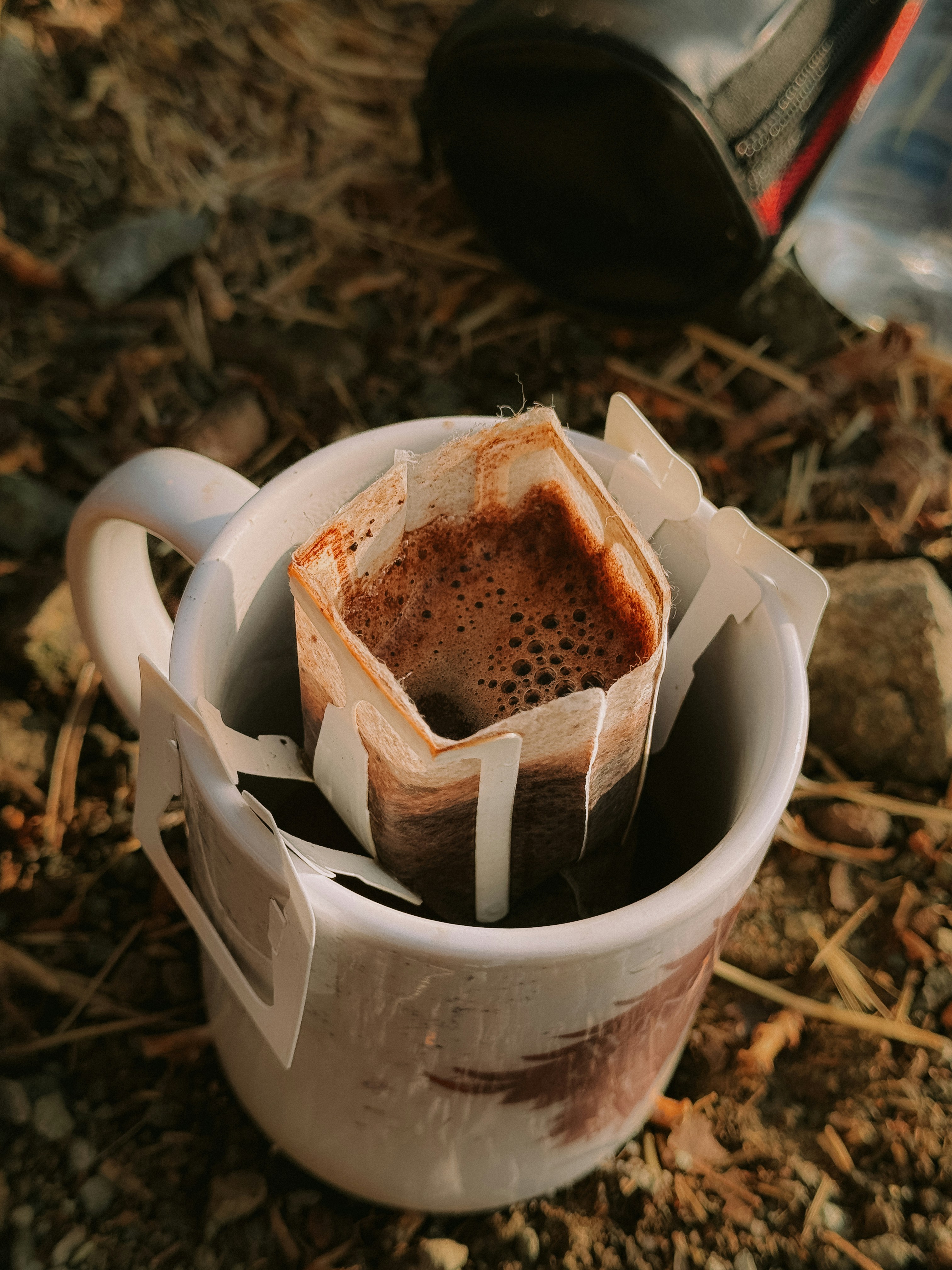 Drip coffee bag brewing in a white mug outdoors