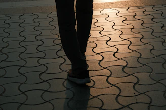 Person walking on a patterned sidewalk at sunset.