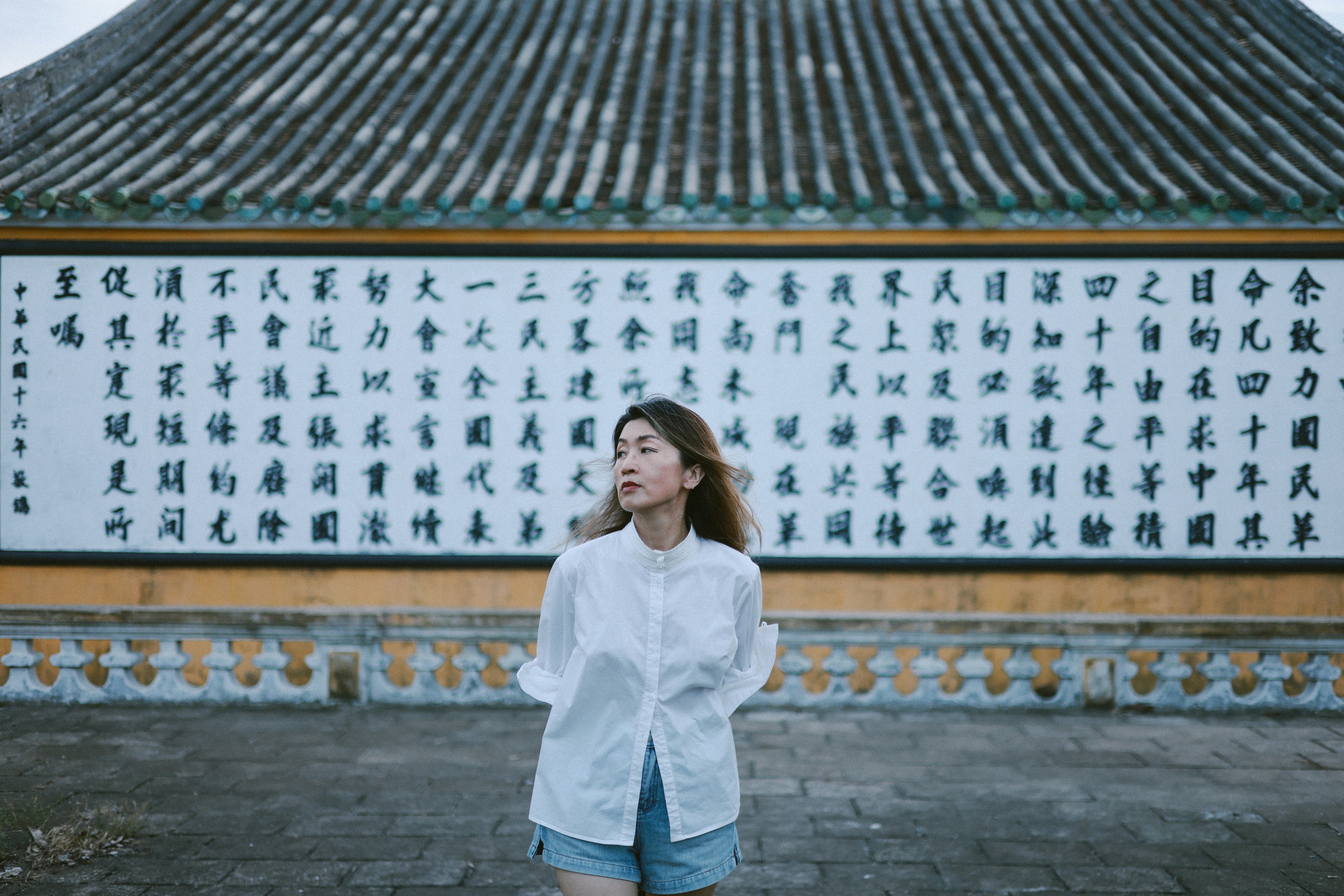 Woman in white shirt stands before wall with asian calligraphy.