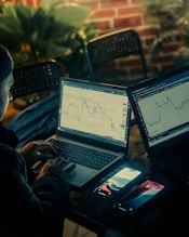 Person working on laptops with stock charts displayed.