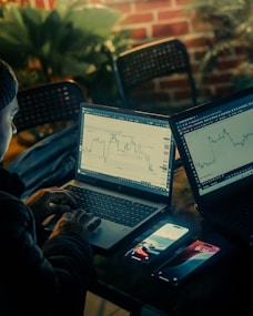 Person working on laptops with stock charts displayed.