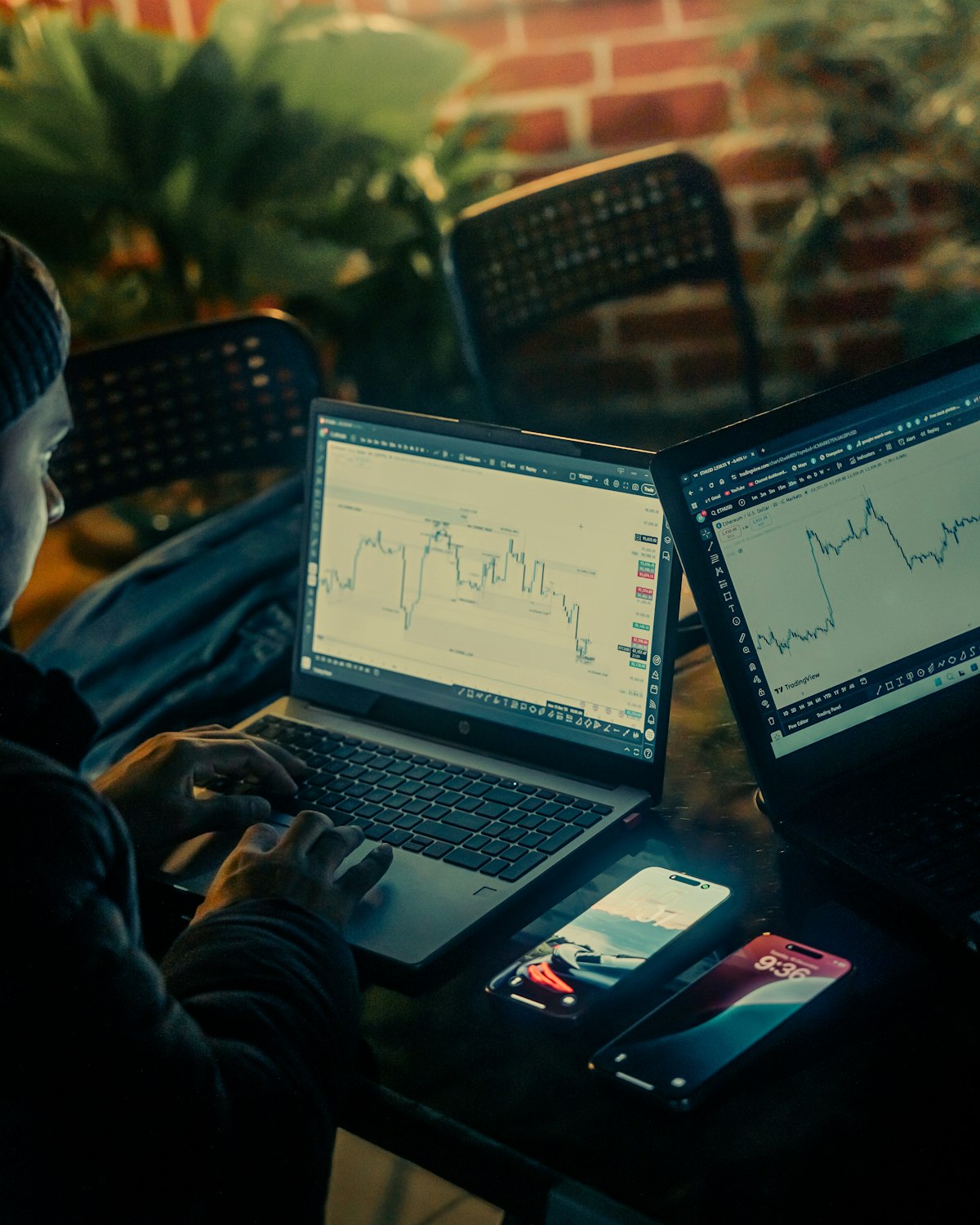 Person working on laptops displaying financial stock charts and data analytics