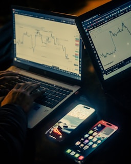 Hands typing on laptops with stock charts displayed.