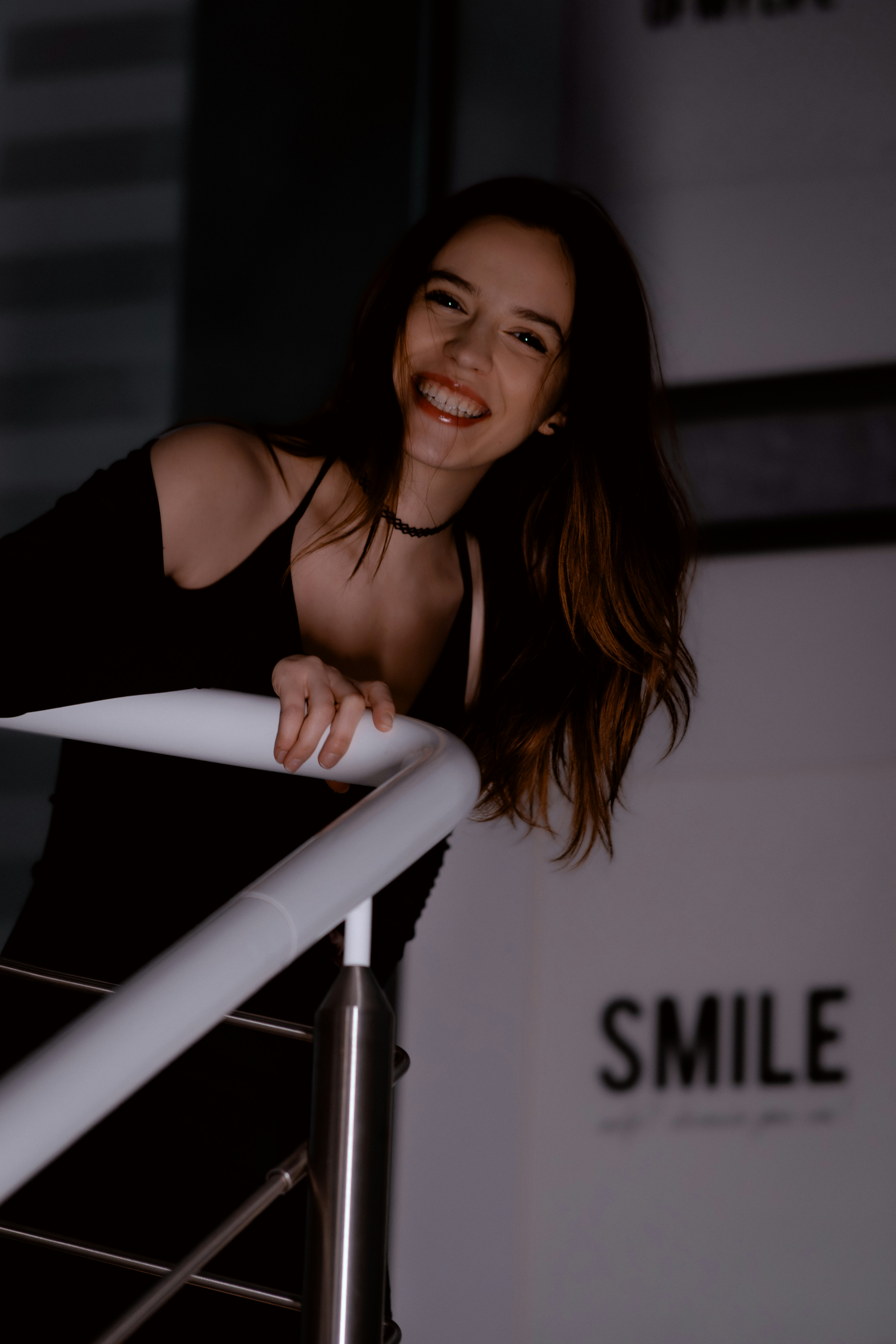 A smiling woman in a black dress leans on railing.