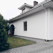 A white house with green bushes and paved walkway
