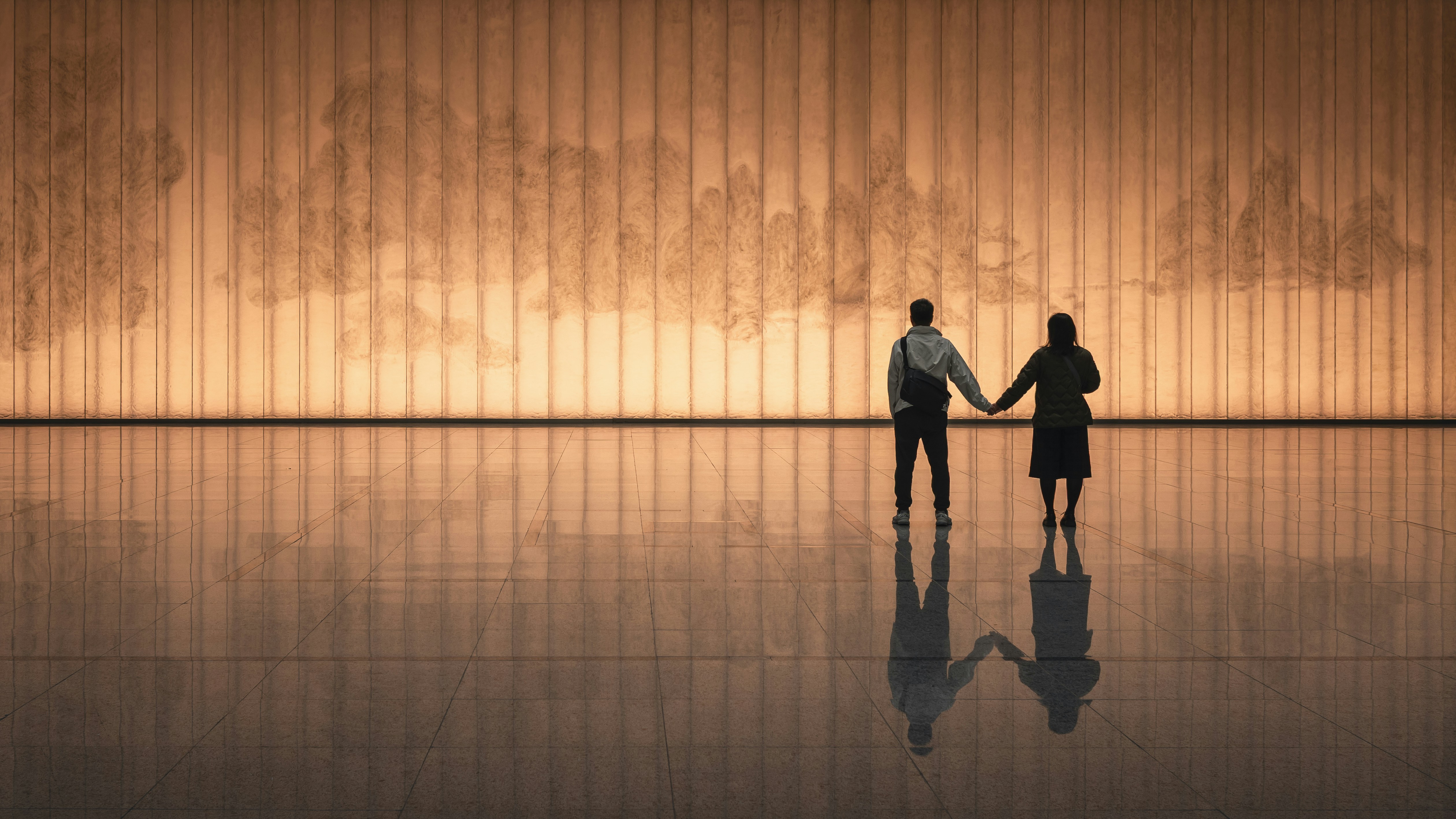 Couple holding hands in front of illuminated wall