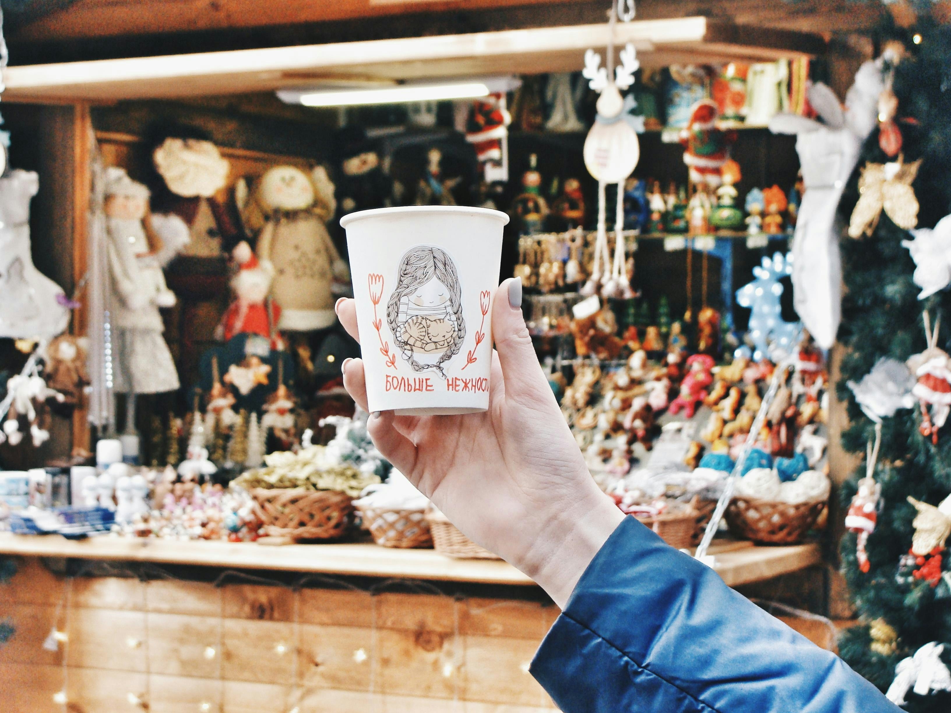 A person holding a festive cup of mulled wine at a Christmas market stall in winter