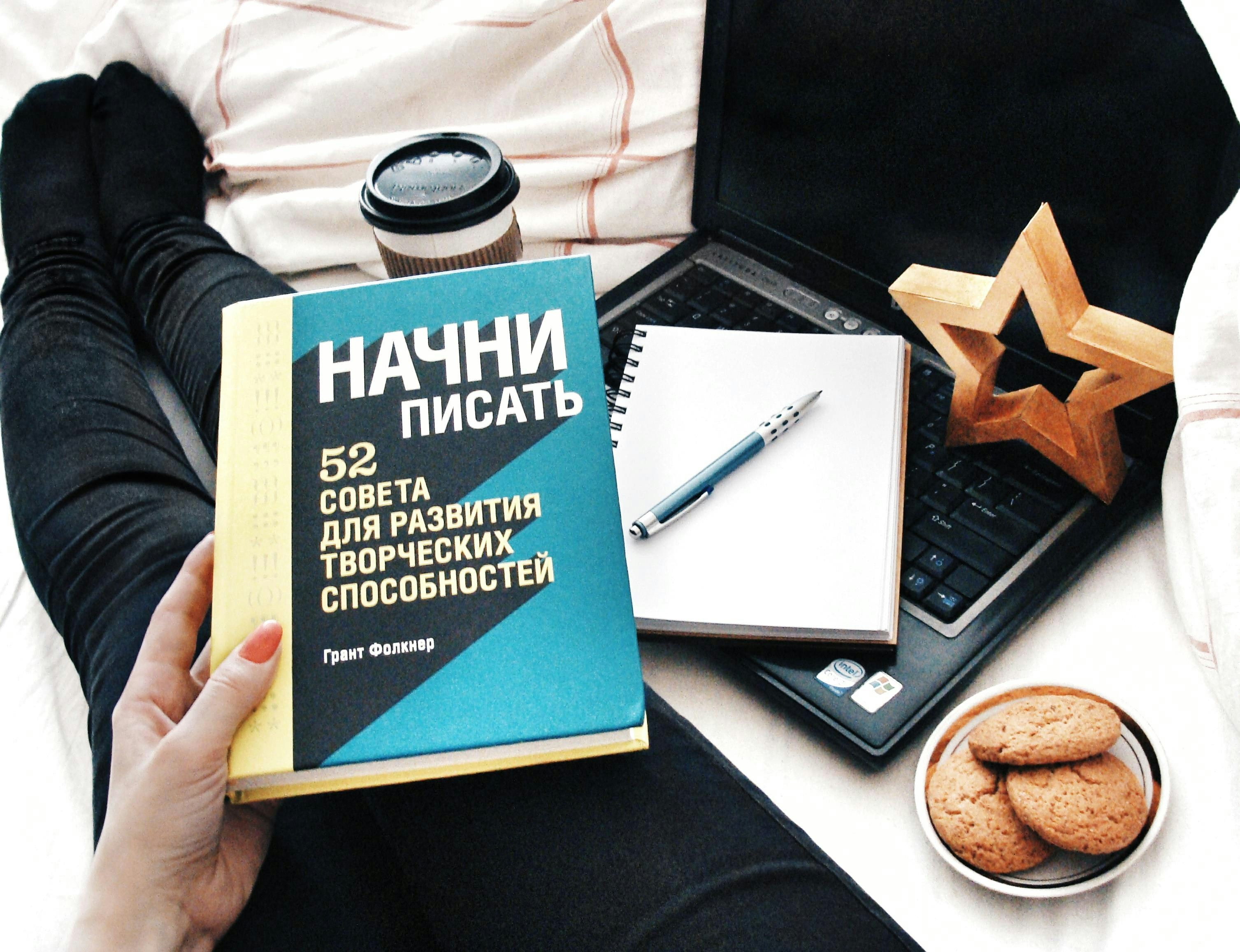 Person reading a book with laptop and coffee