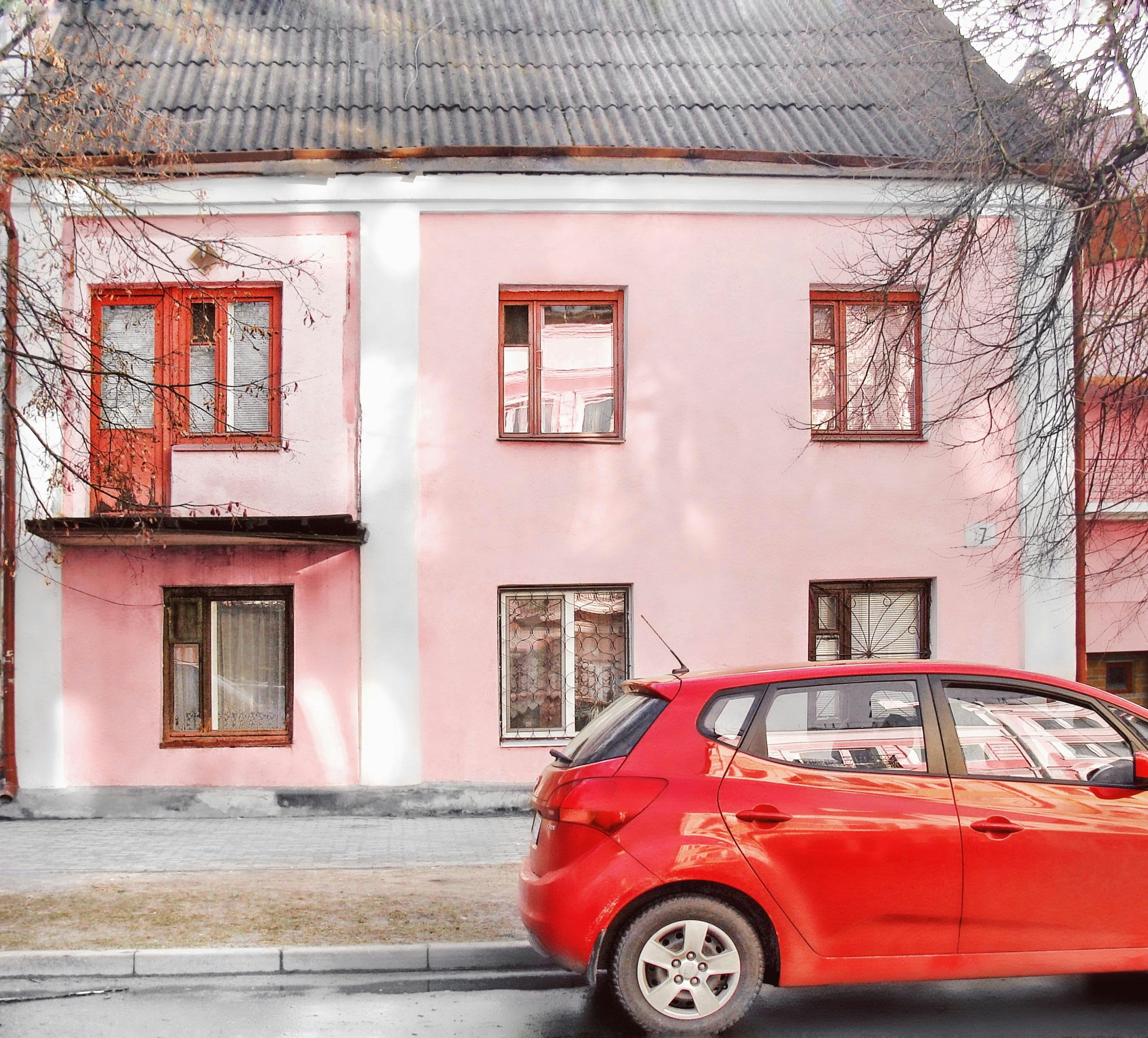 Red car parked in front of a pink building.