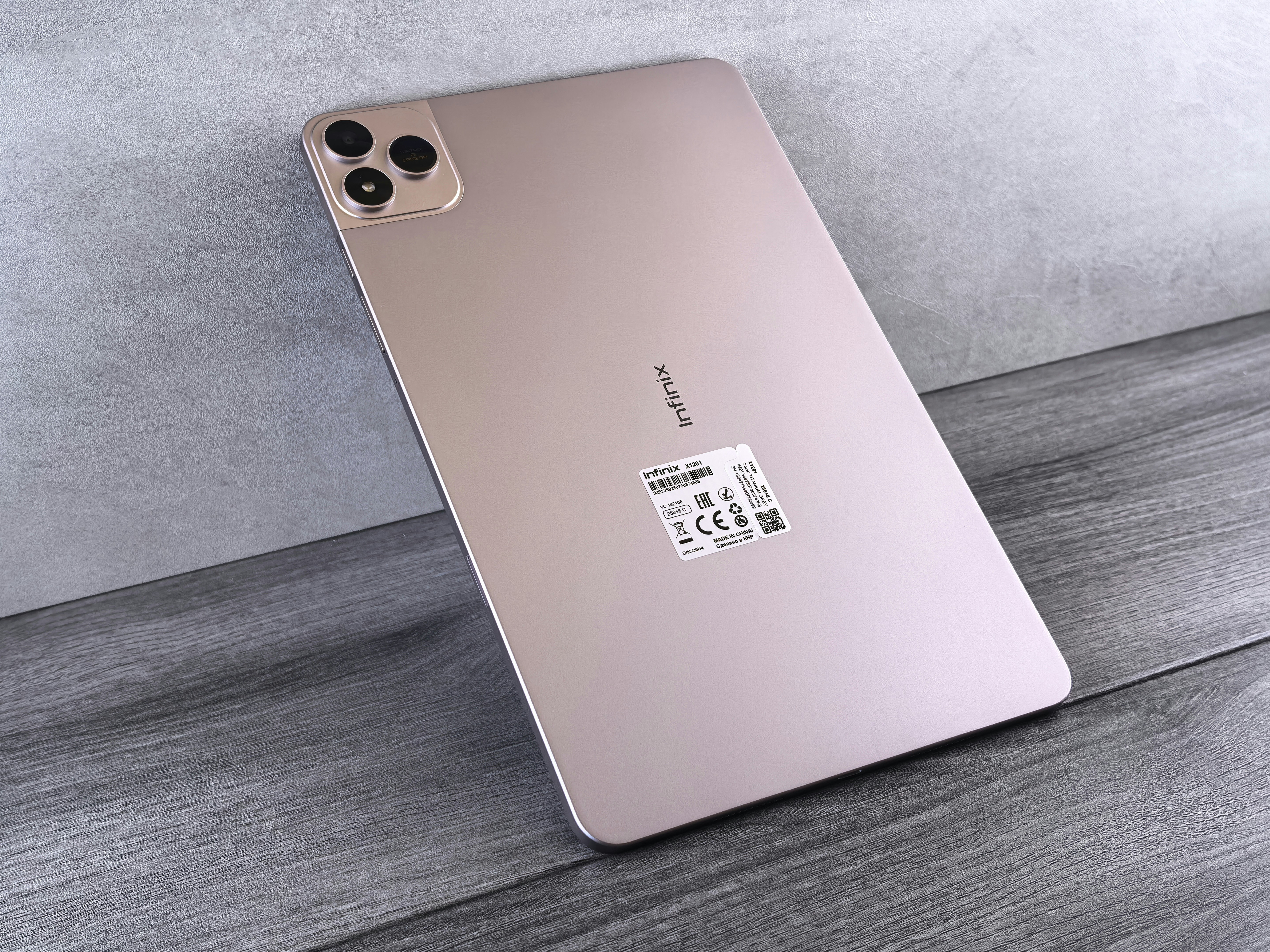 Une tablette en or rose est appuyée contre un mur texturé.