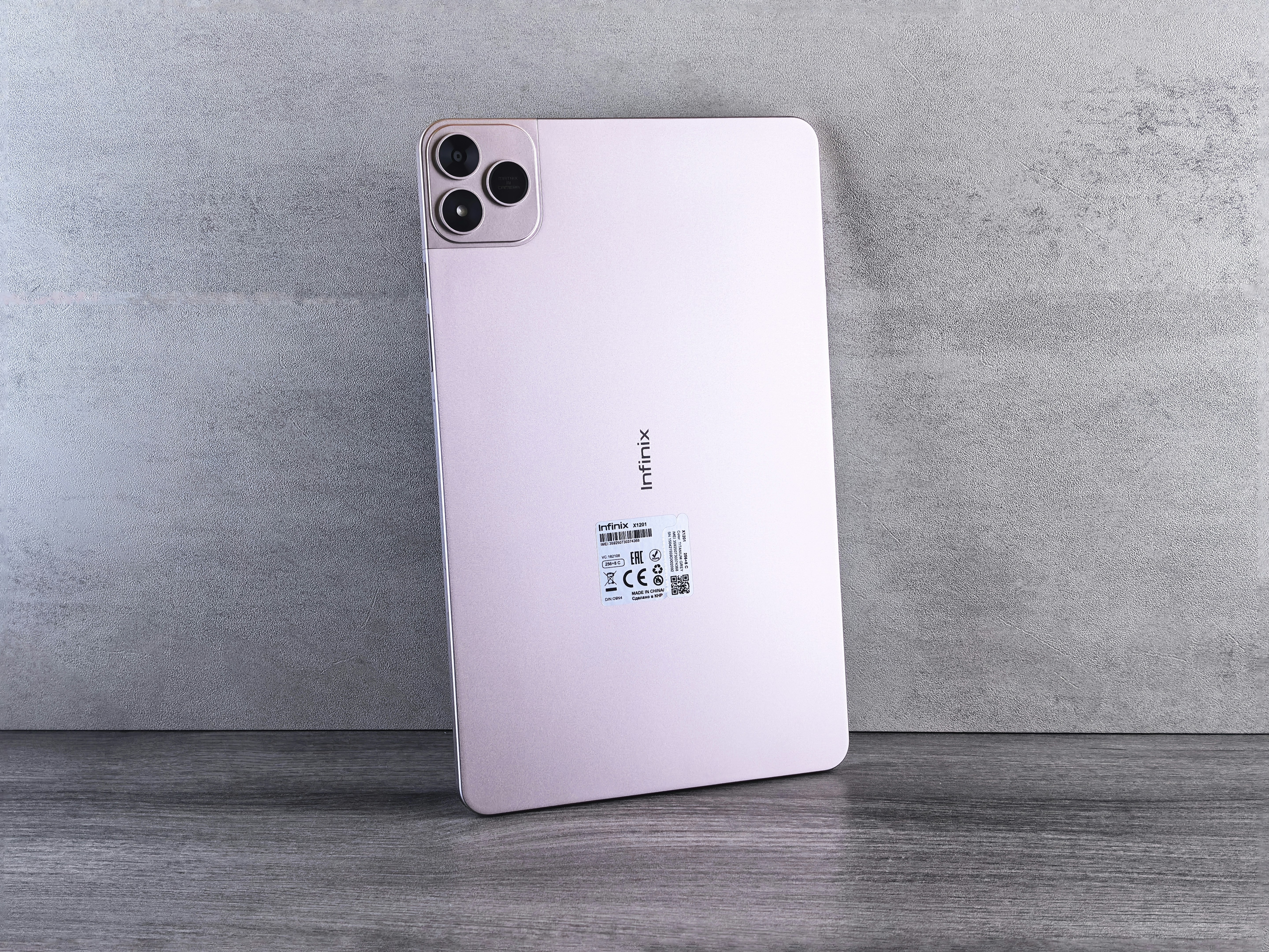 Tablette rose avec système triple caméra sur fond gris.