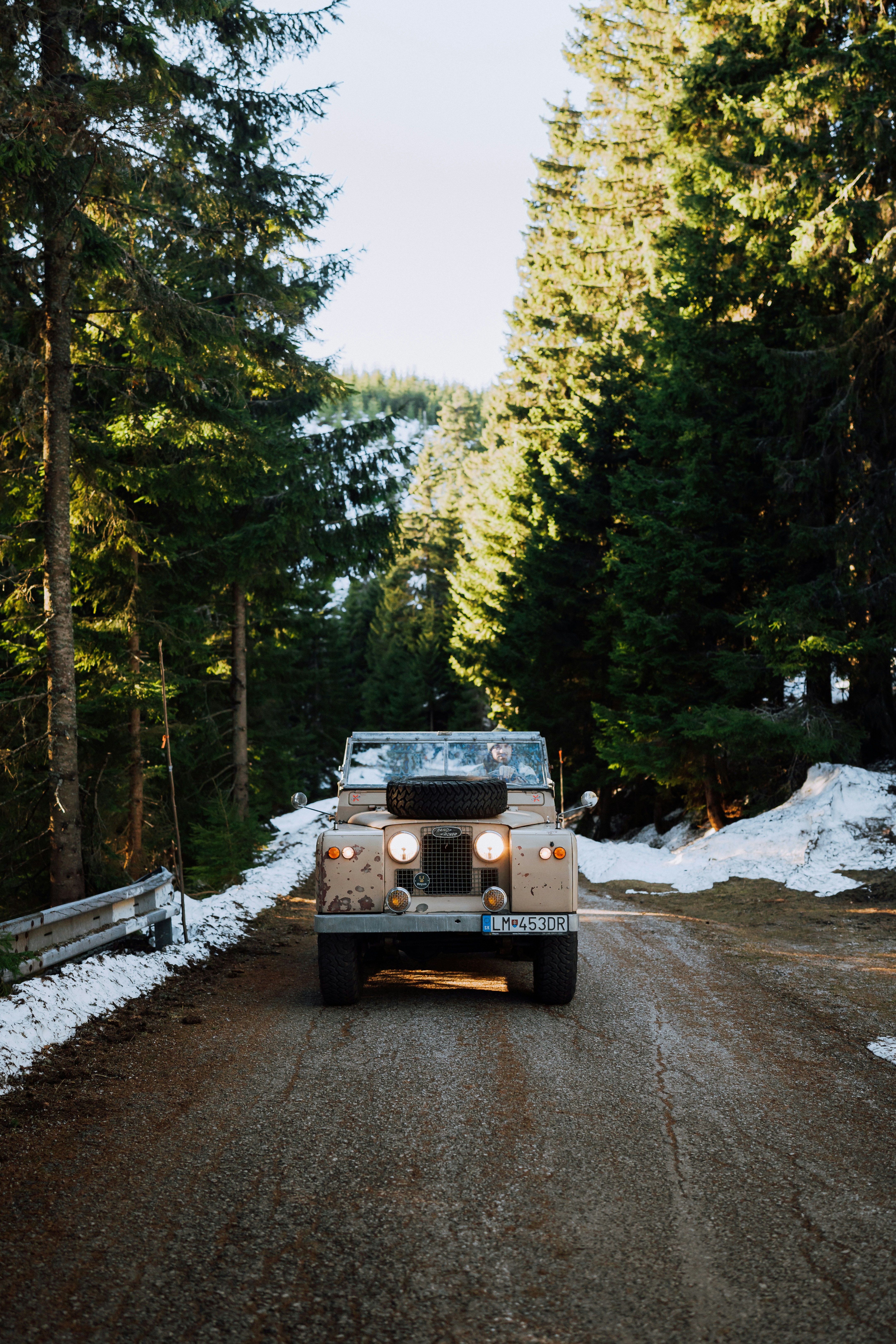 A vintage vehicle drives on a forest road.