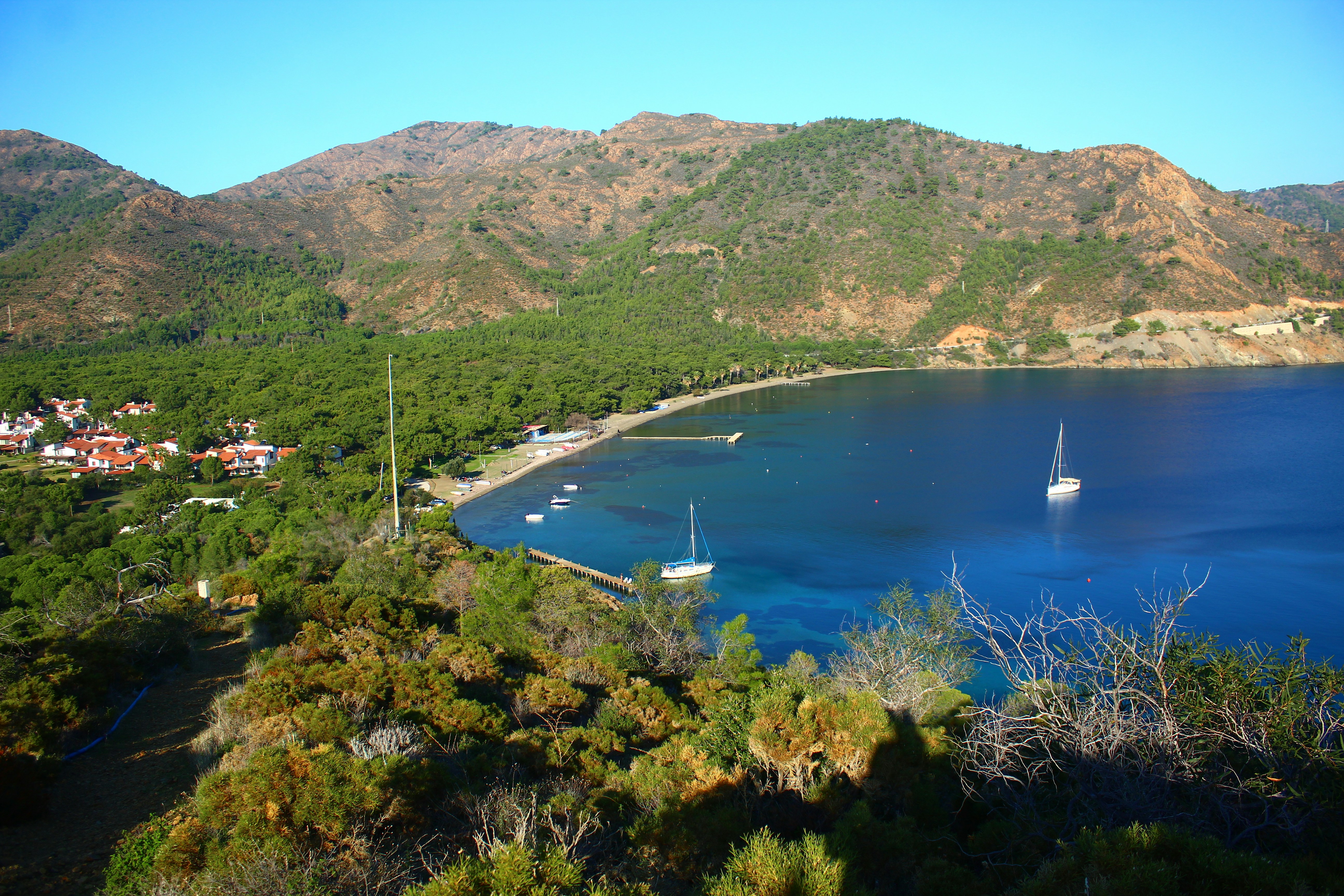Sailboats moored in a tranquil bay with coastal village.