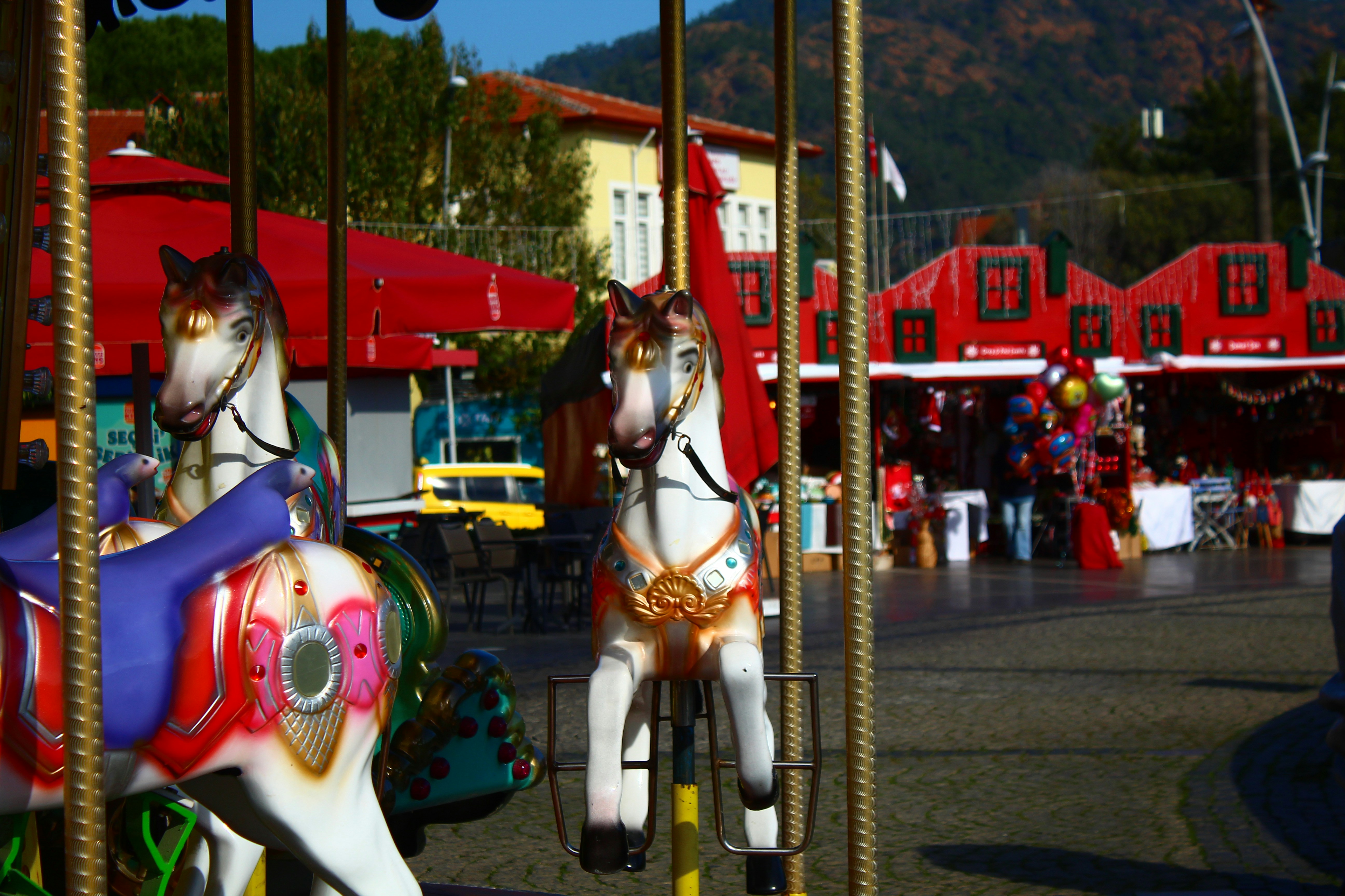 Carousel horses at a sunny outdoor amusement park.