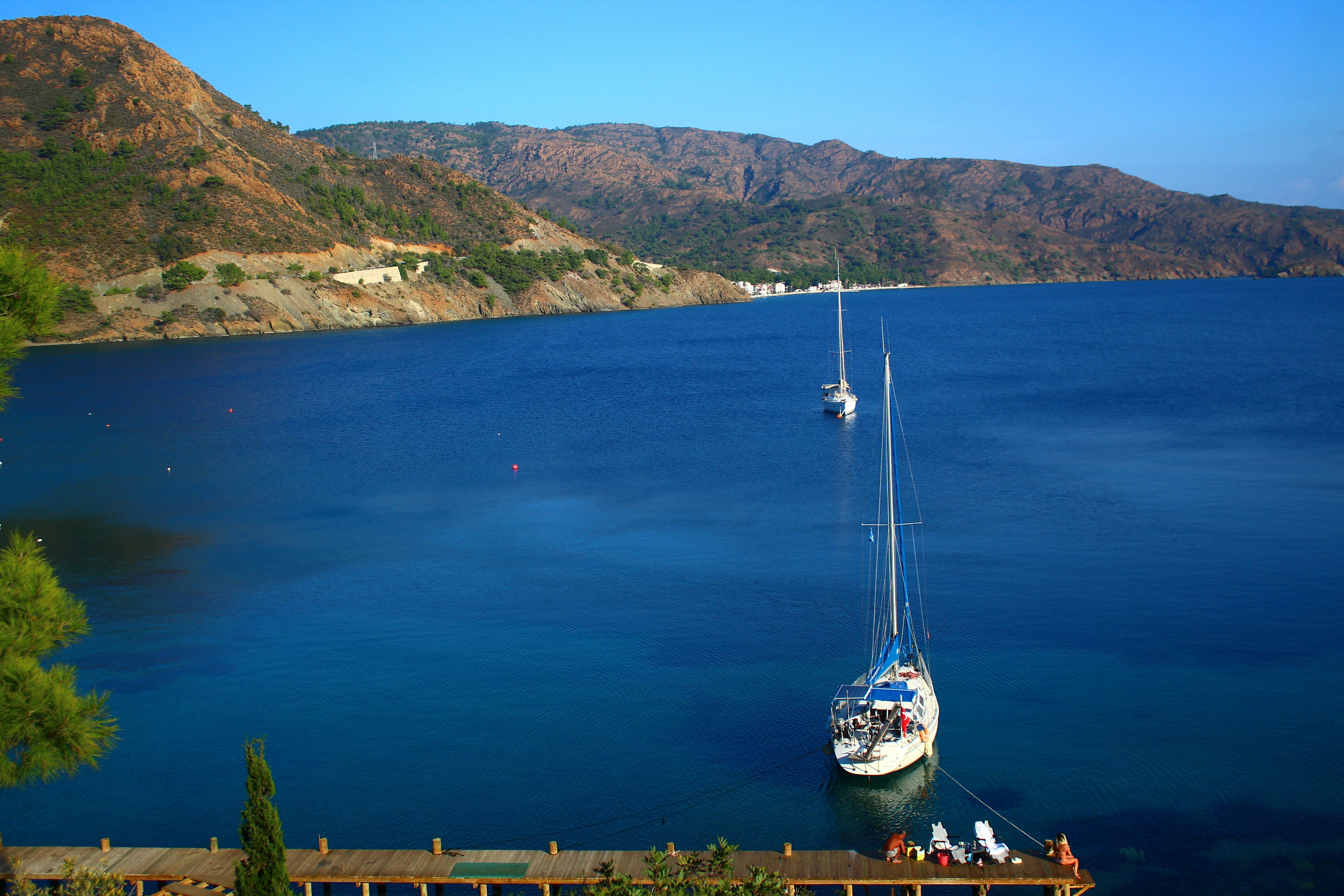 Sailboats anchored in a calm blue bay with mountains.