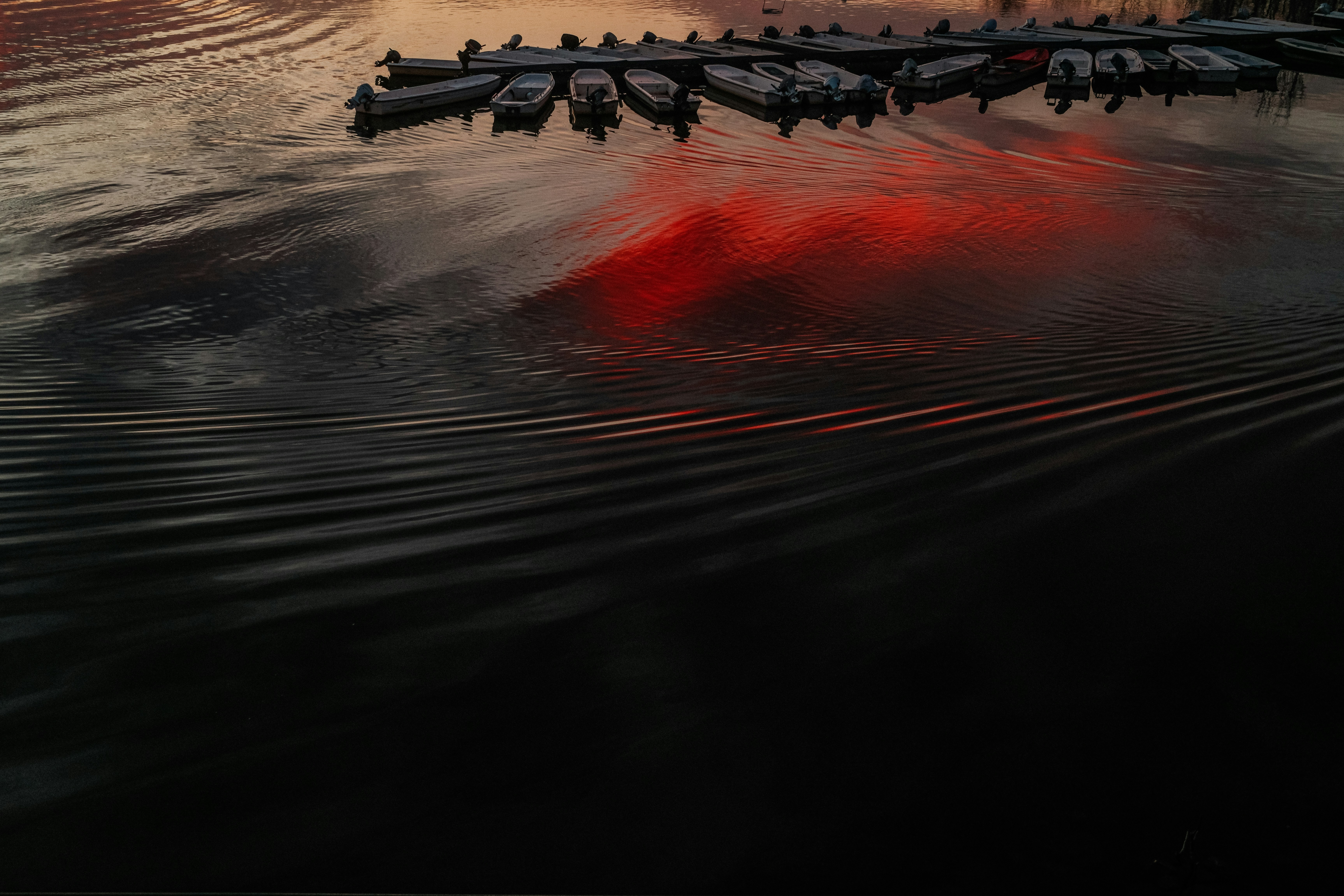 Boats docked at sunset with red reflections on water.