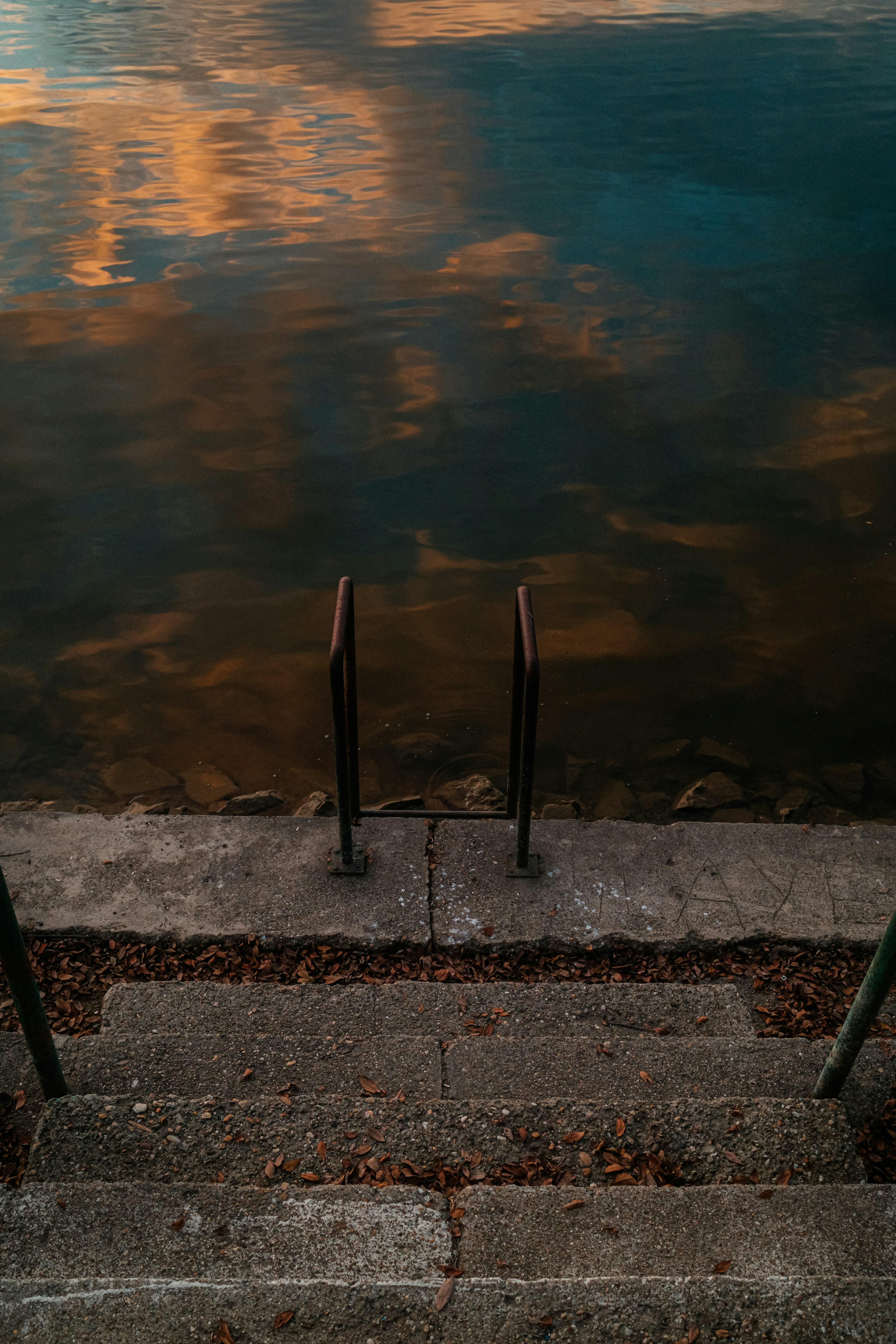 Concrete stairs leading to a reflective lake at sunset.