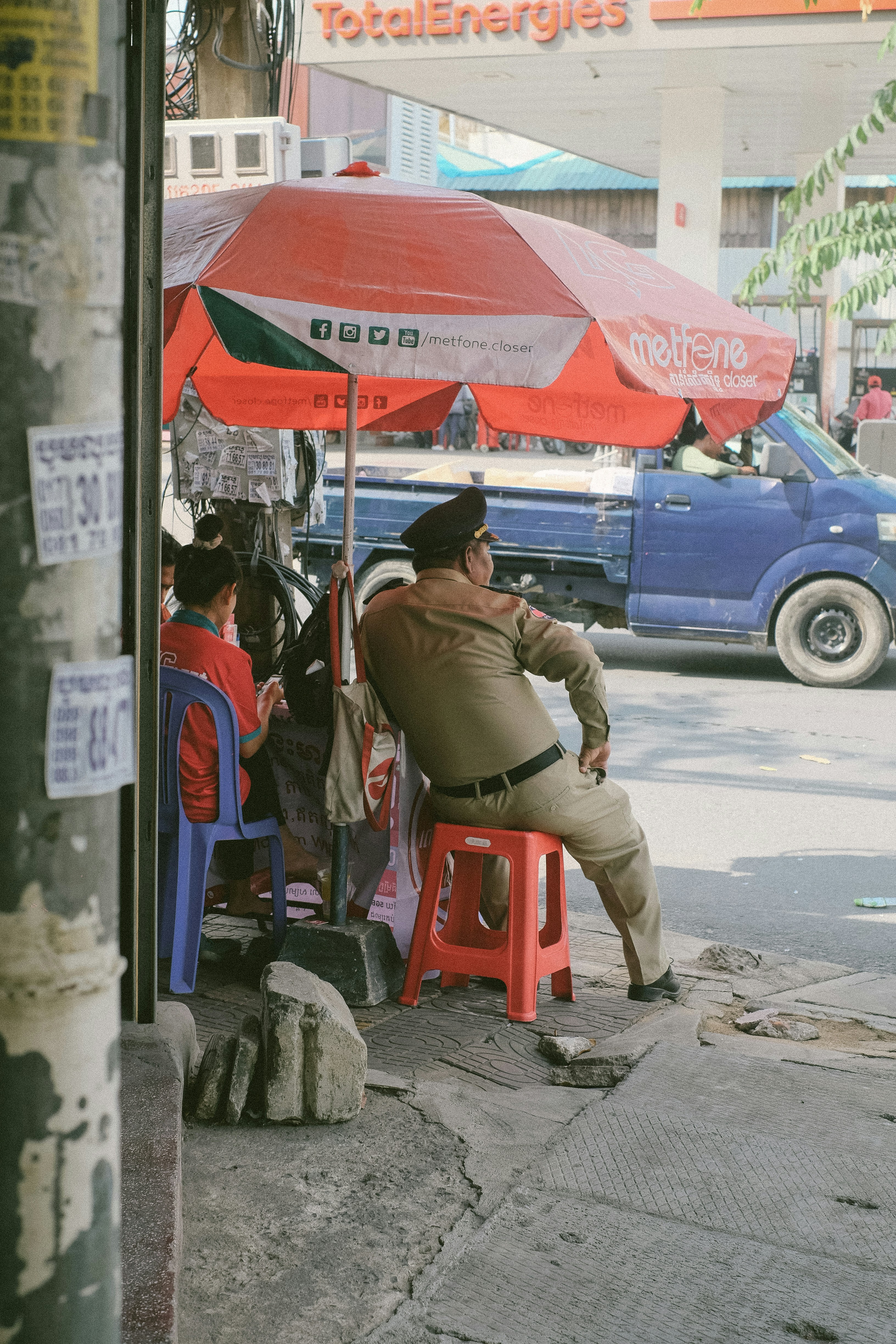 Hombre uniformado sentado bajo un paraguas en un puesto junto a la carretera.