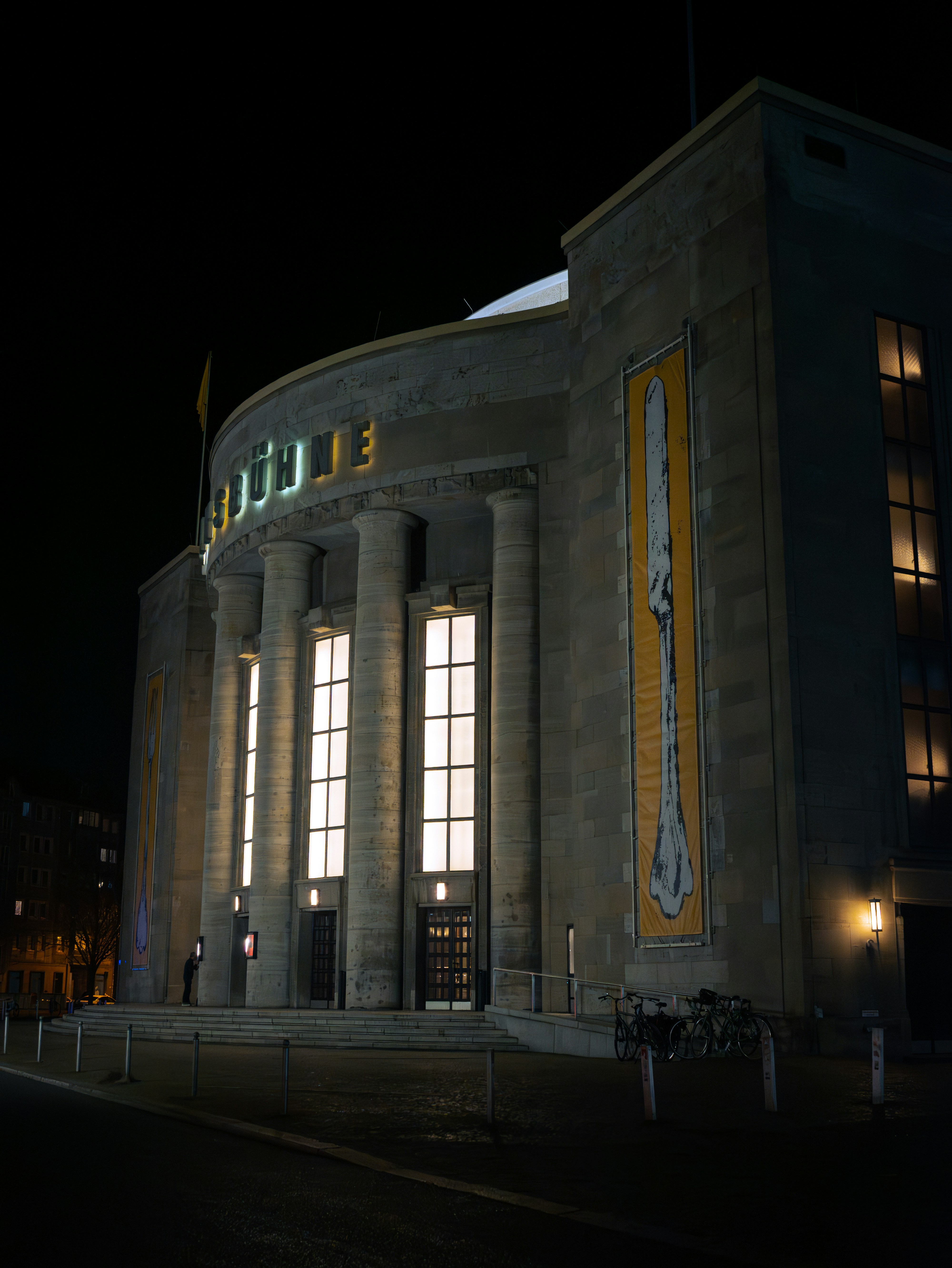 A monumental theater building in Berlin illuminated against the night sky. Night at the Museum style. The Volksbühne theater in Berlin photographed at night with dramatic lighting.