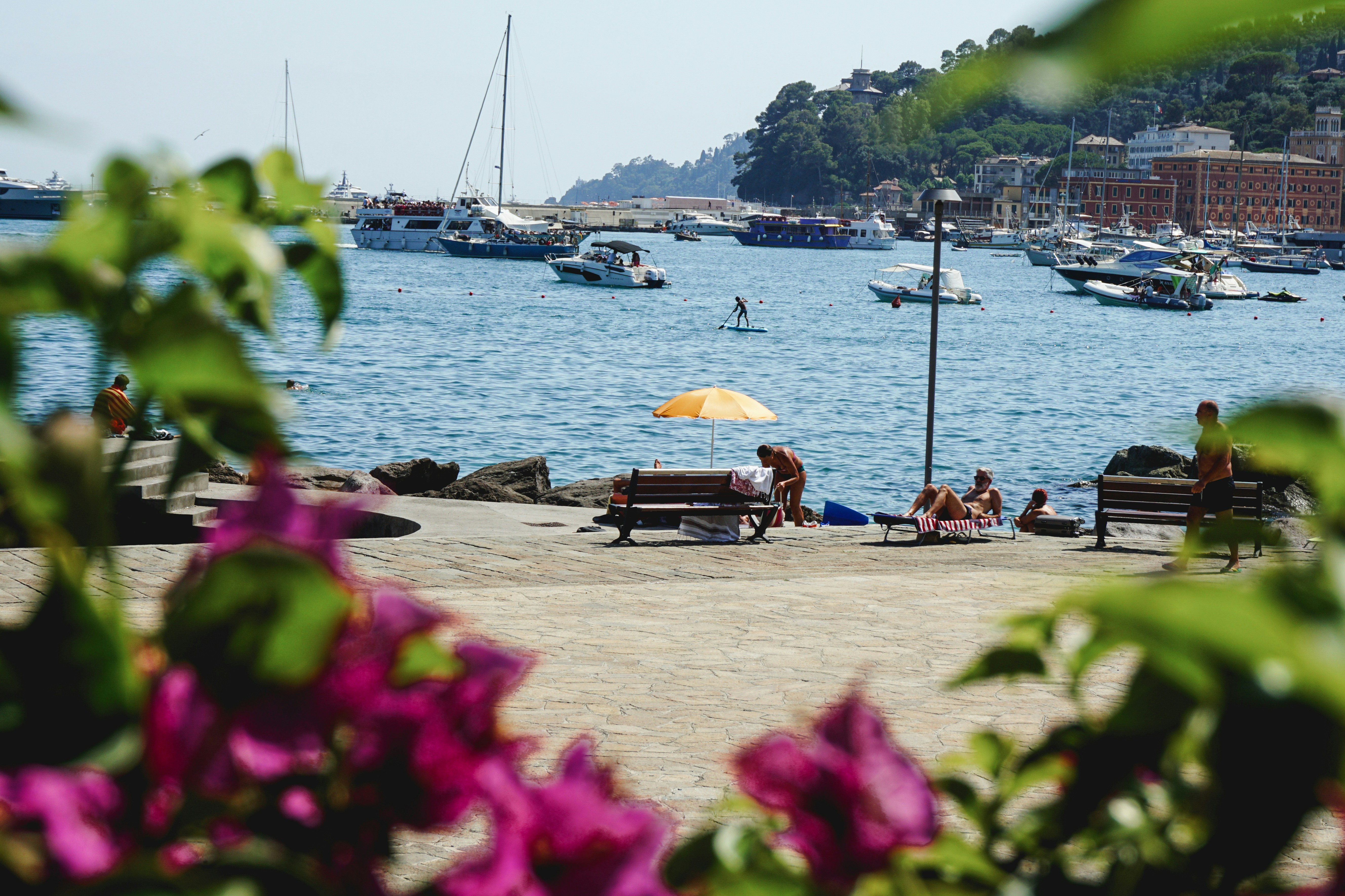 Boats in a harbor with people relaxing on shore.