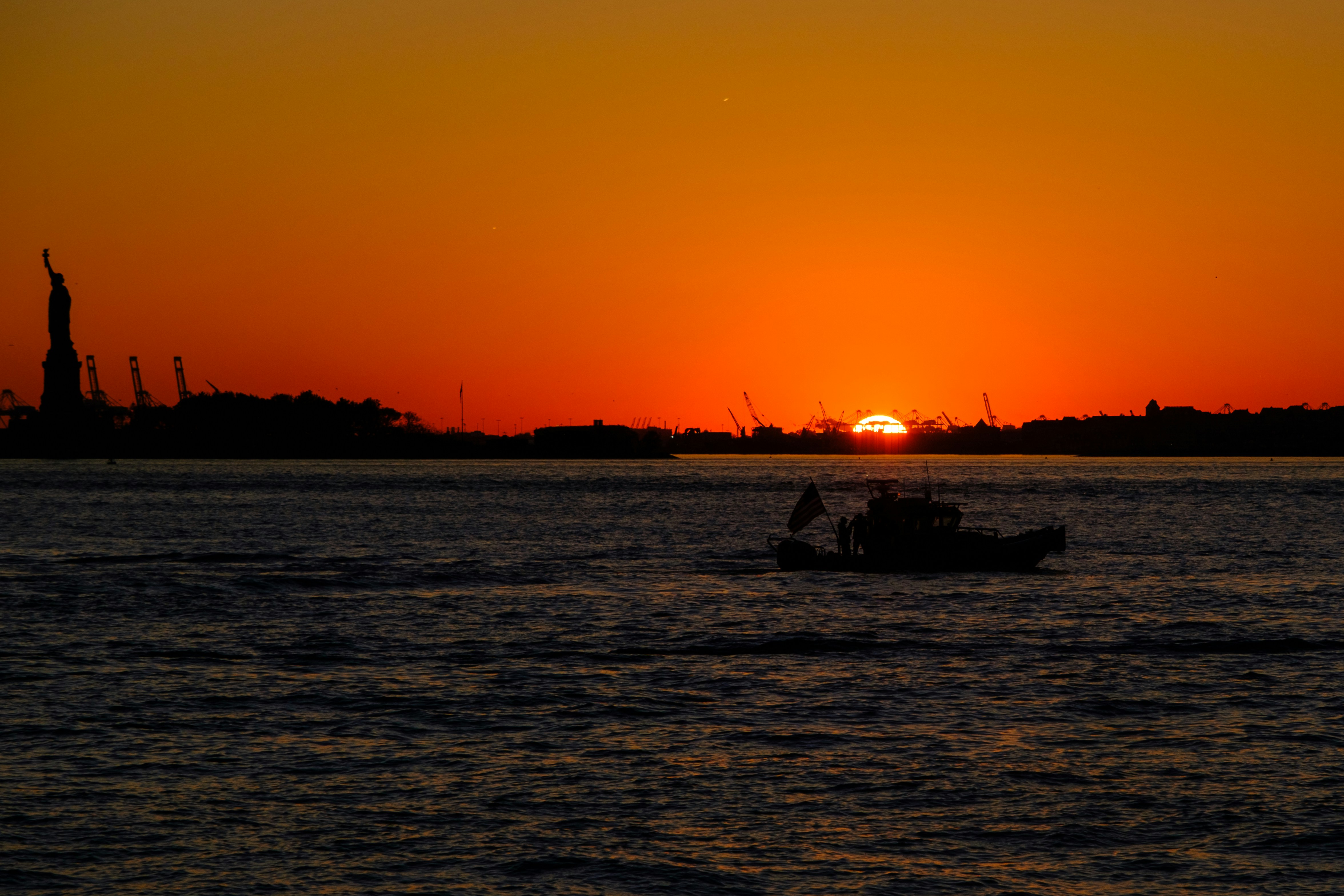 Sunset over water with statue of liberty silhouette