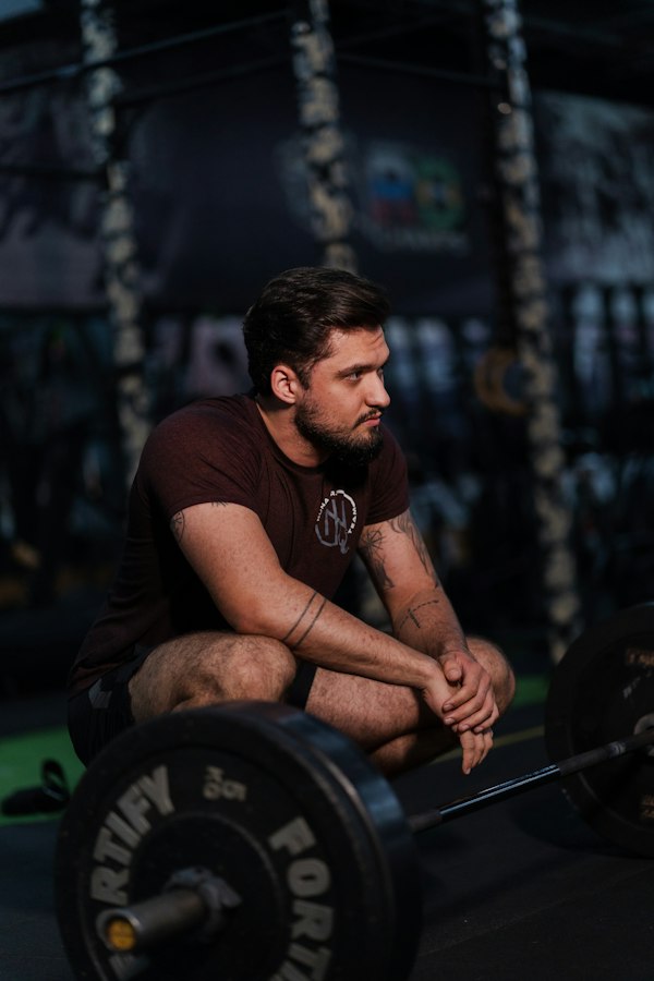 Caleb, 27, resting beside a loaded barbell after a deadlift session at FitForge