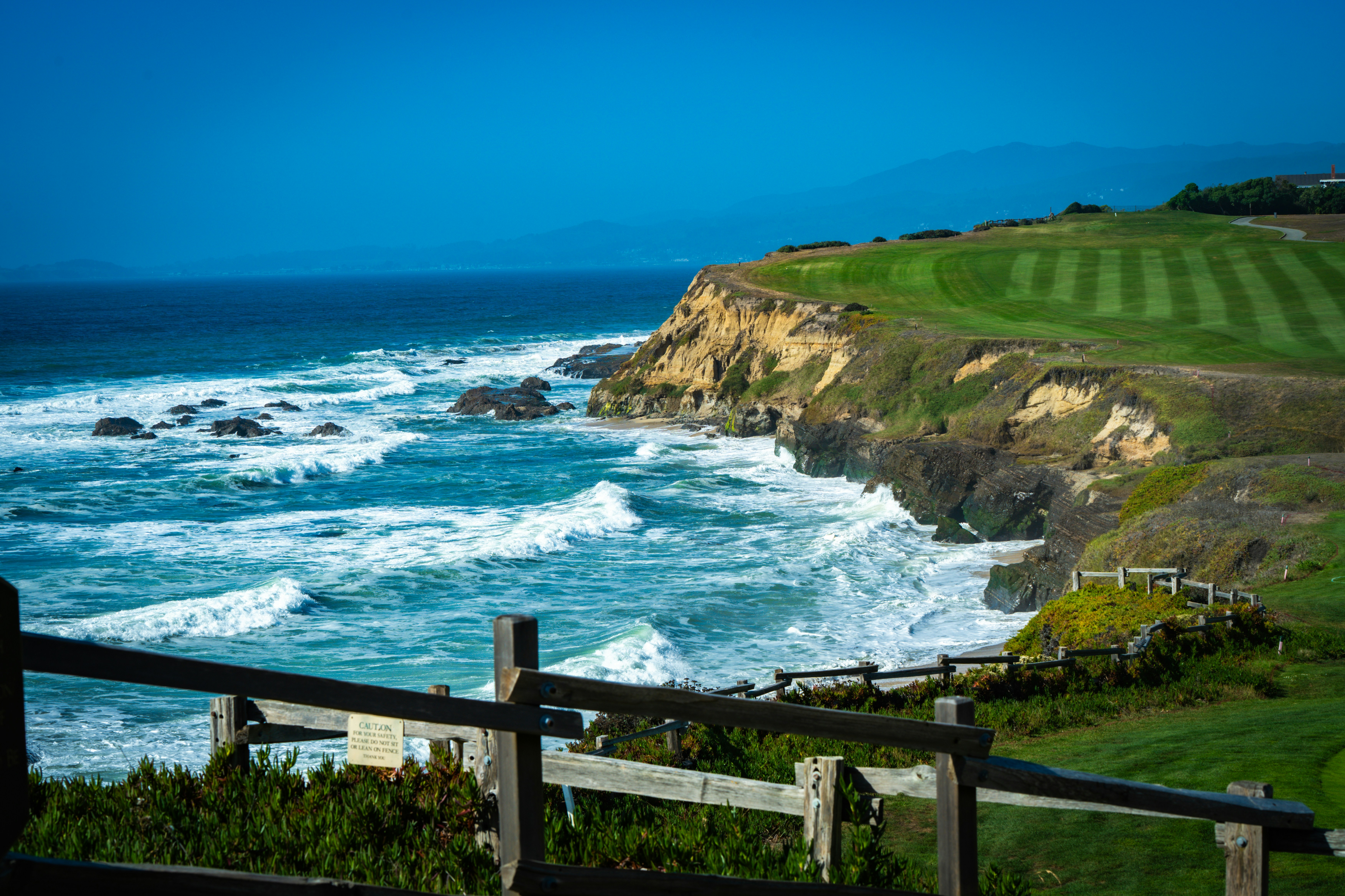 Waves crash on a rocky coastline with a golf course.
