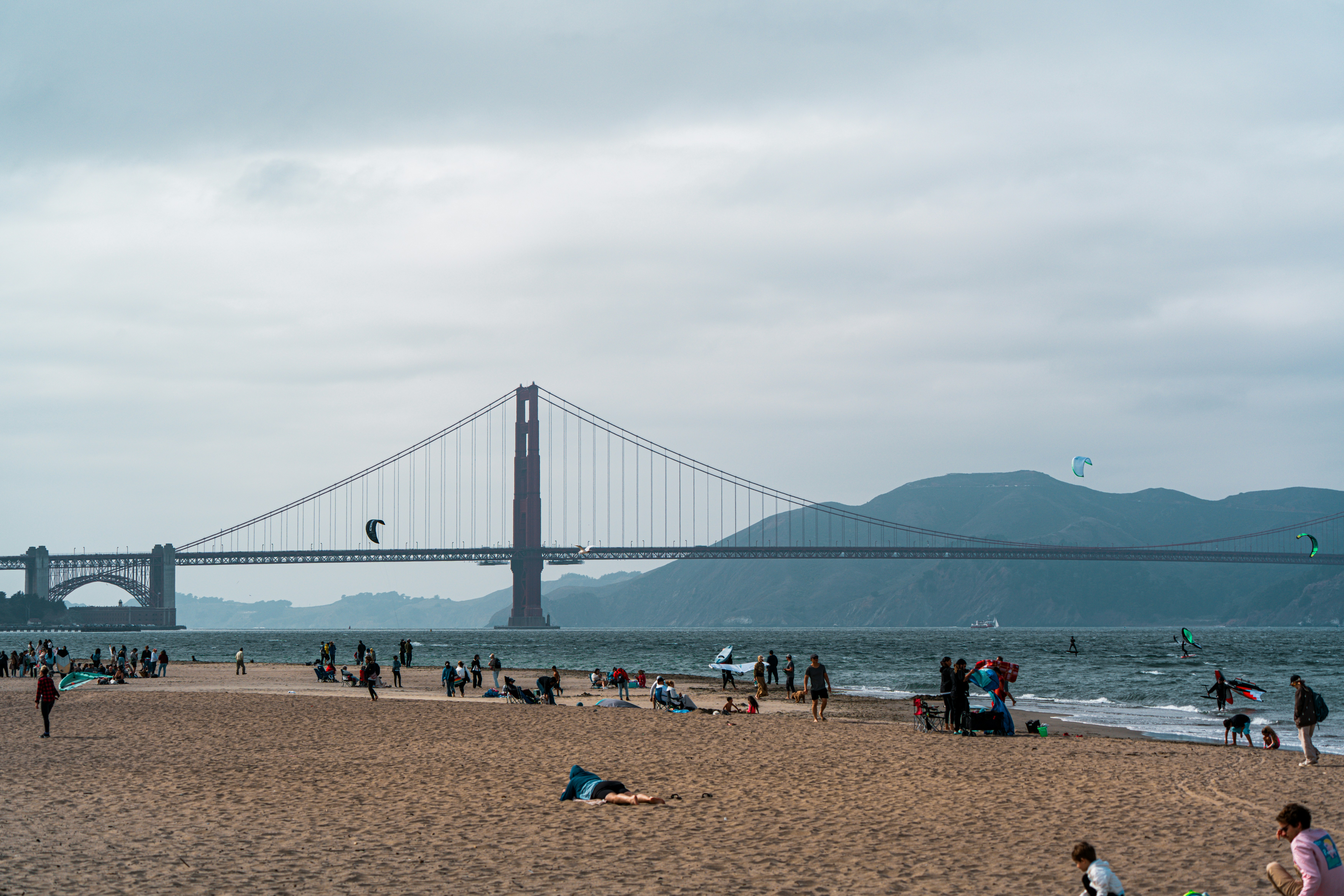People relax on a sandy beach with golden gate bridge.