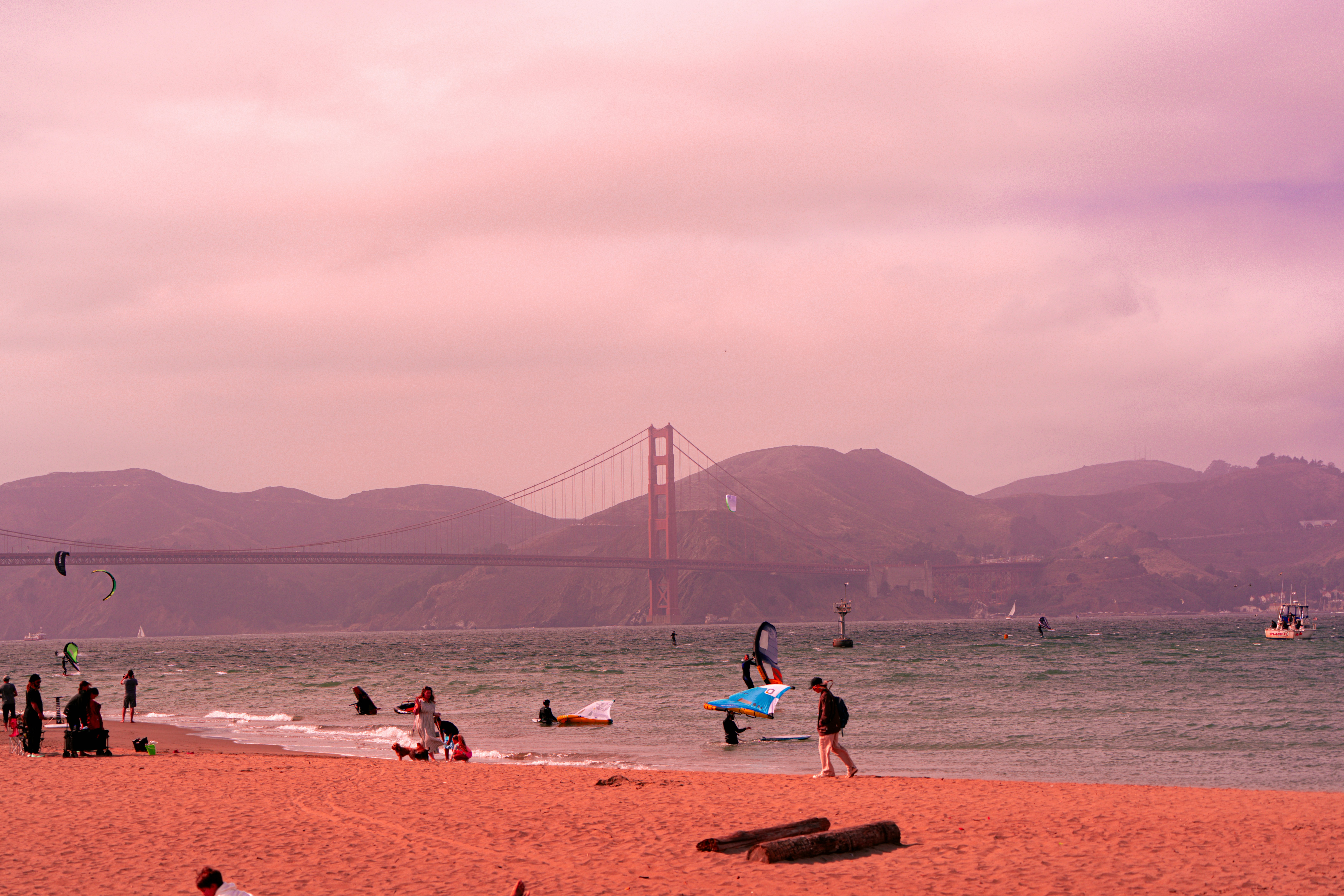 People on a beach with golden gate bridge in background.