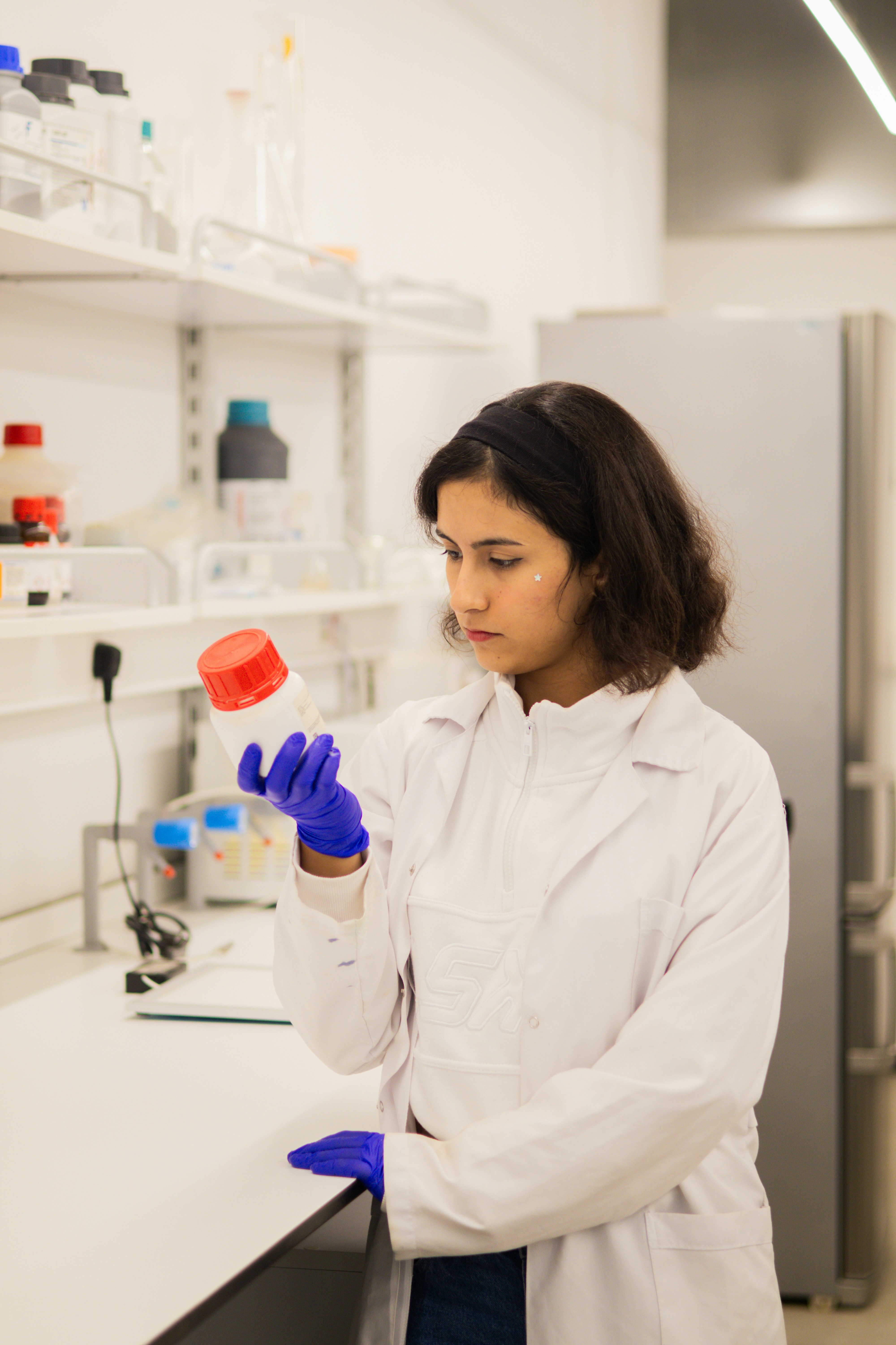 Scientist in lab coat holds bottle with red cap.