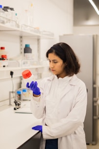 Scientist in lab coat holds bottle with red cap.