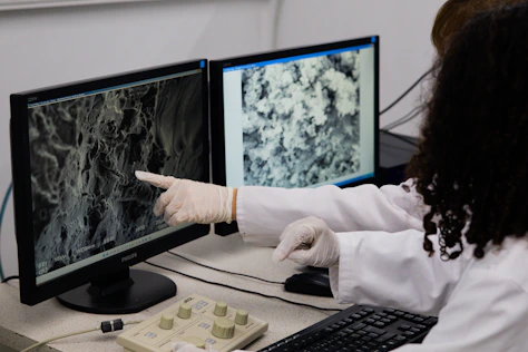 Scientist points to microscopic view on computer screen.
