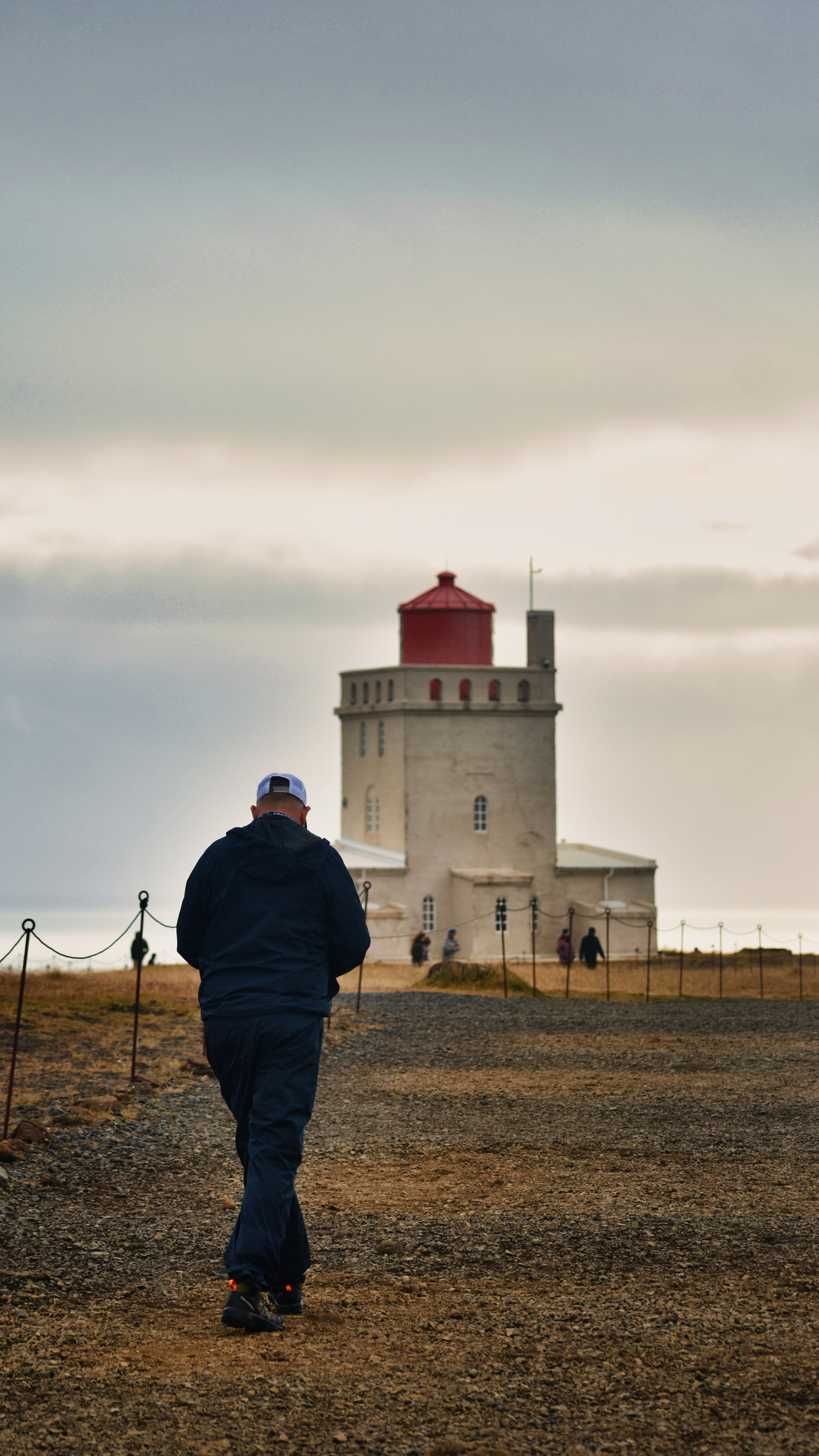 Ein Mann geht an einem bewölkten Tag auf einen Leuchtturm zu.