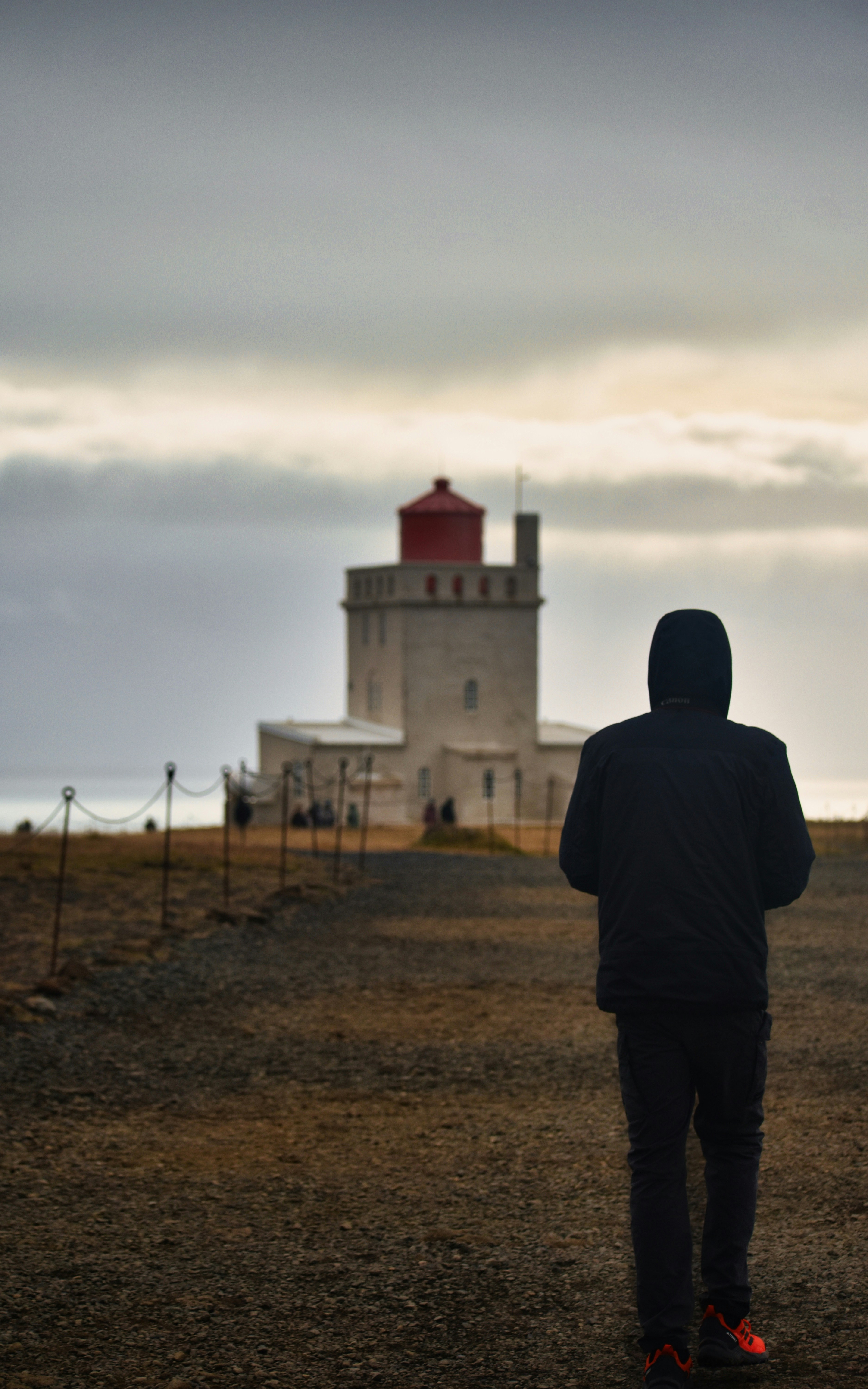 Die Person geht an einem bewölkten Tag auf einen Leuchtturm zu.