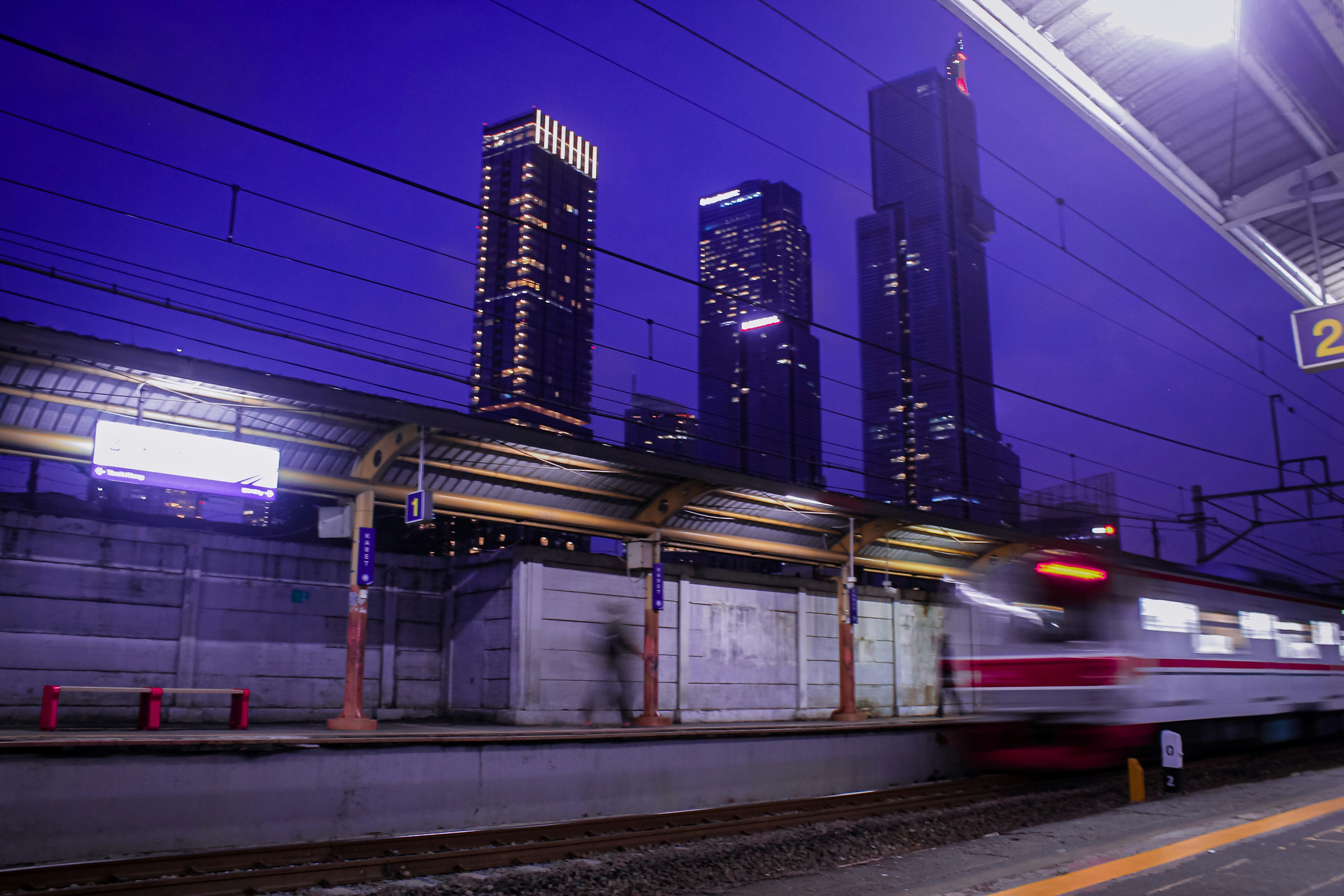 Train passing a station with a city skyline at night