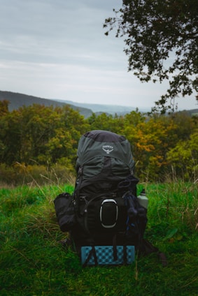 A large backpack sits on grassy ground with hills behind.