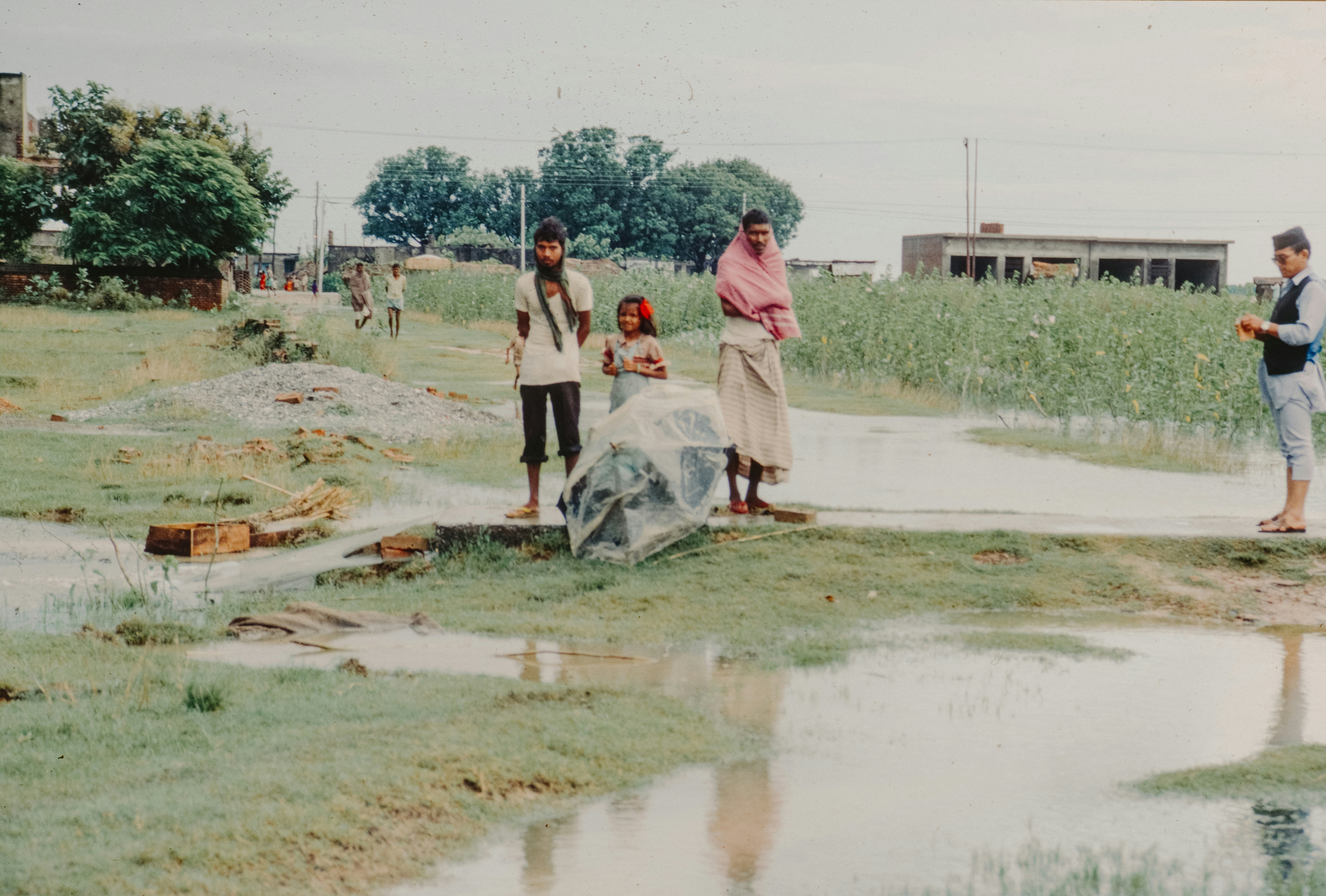 A somber image of villagers gathered in a rural area, looking distressed, with police tape visible in the background.
