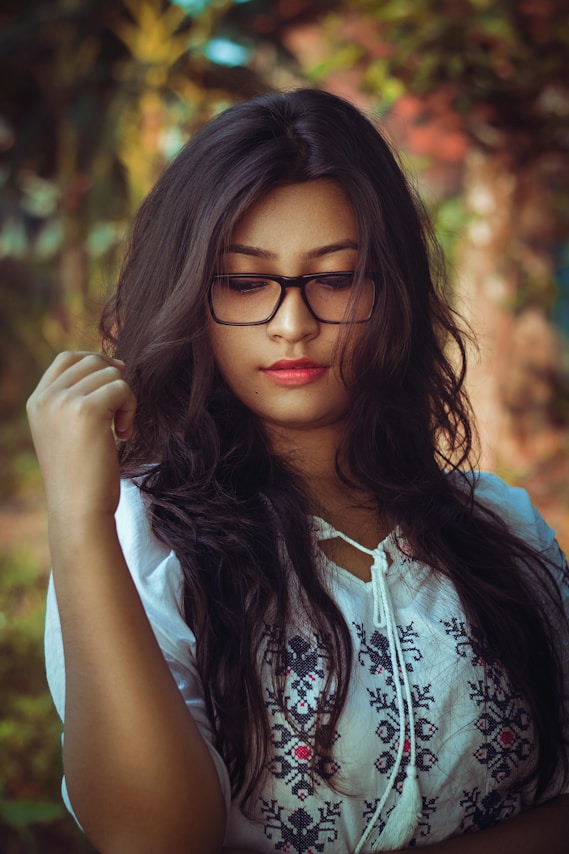 Young woman with glasses looking down thoughtfully downwards outdoors