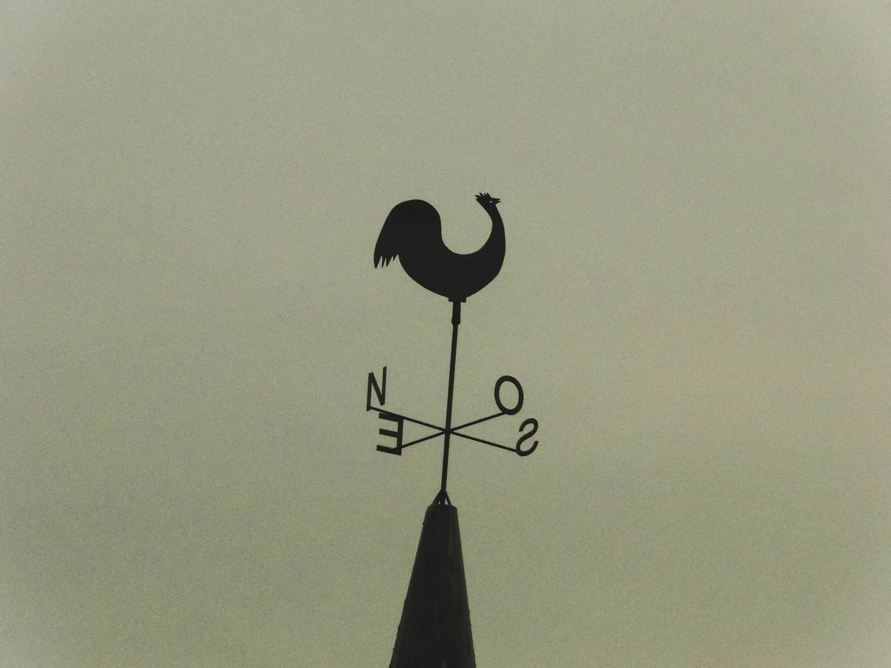 A silhouette of a rooster weather vane on a spire.