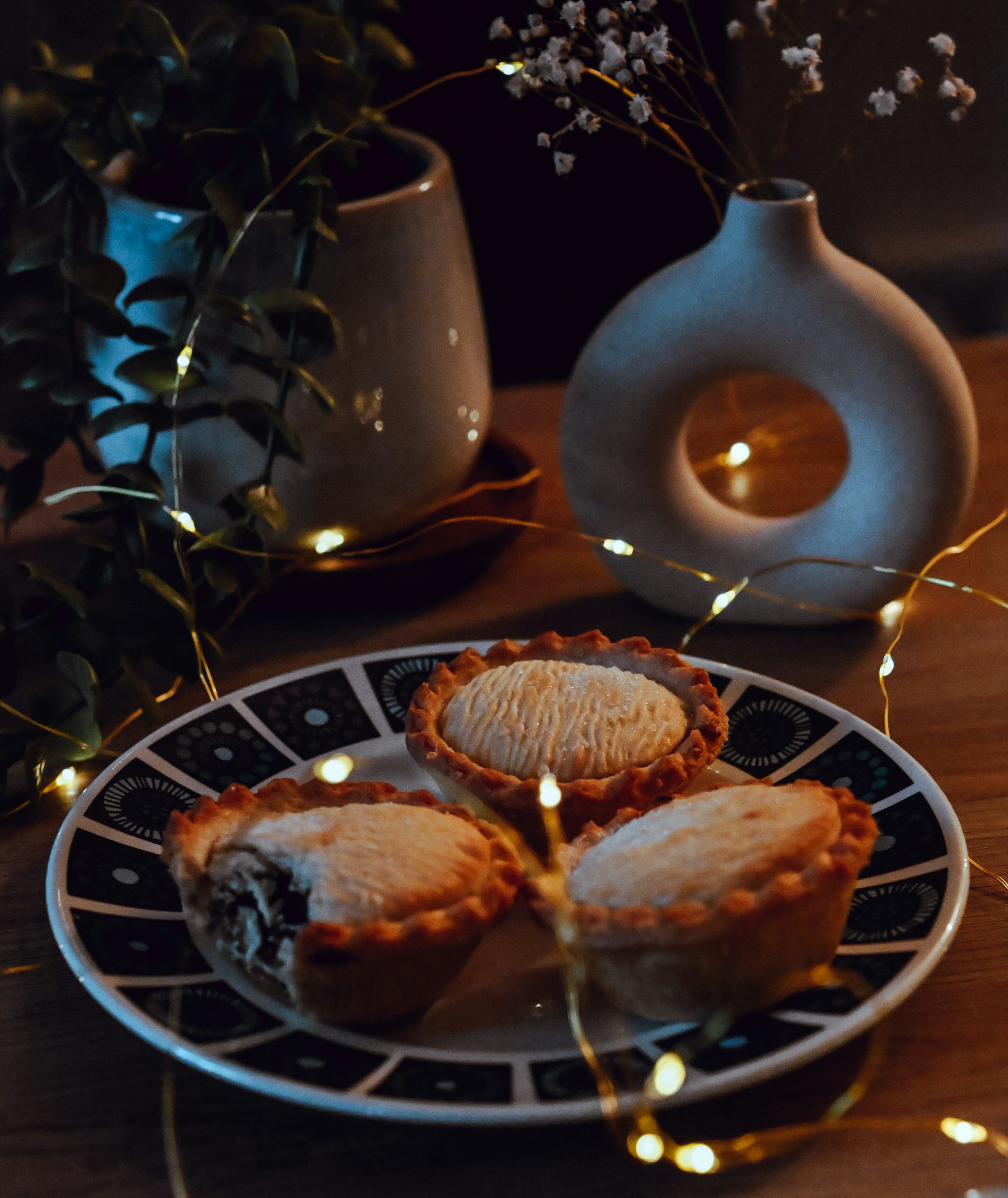 Three mince pies on a patterned plate with fairy lights.