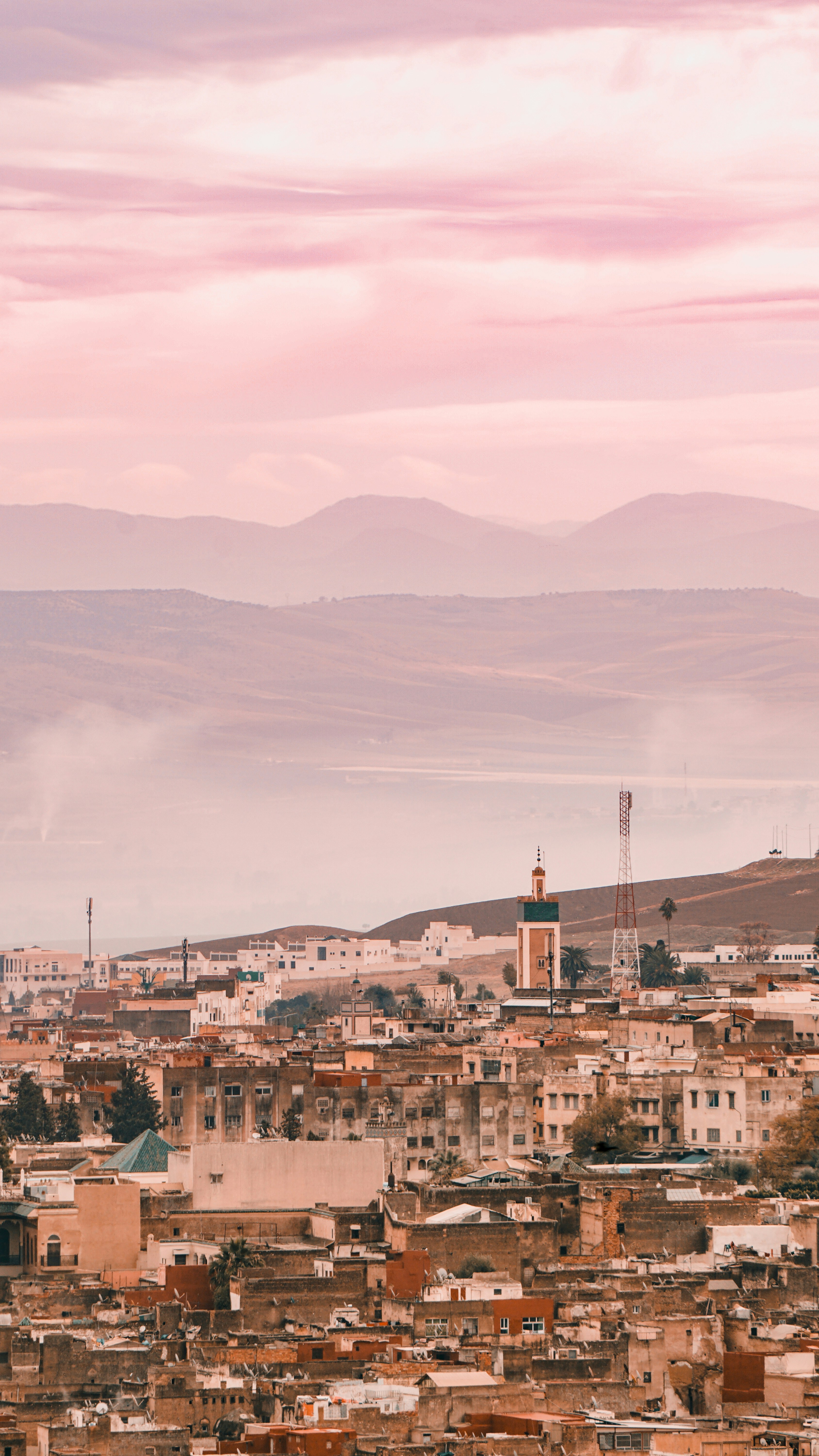 A city skyline with distant mountains under a pink sky.
