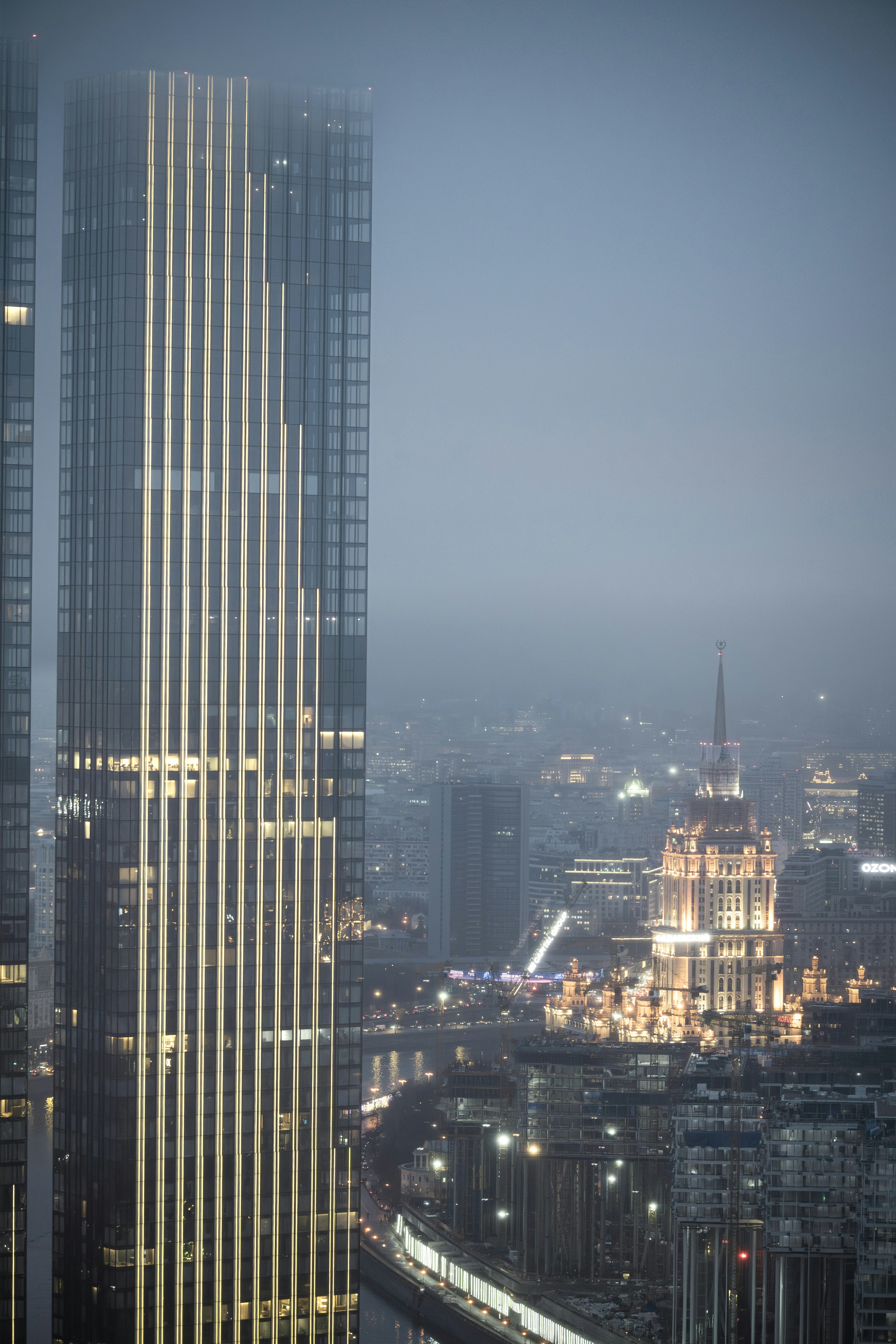 Modern skyscraper illuminated against a foggy cityscape at night