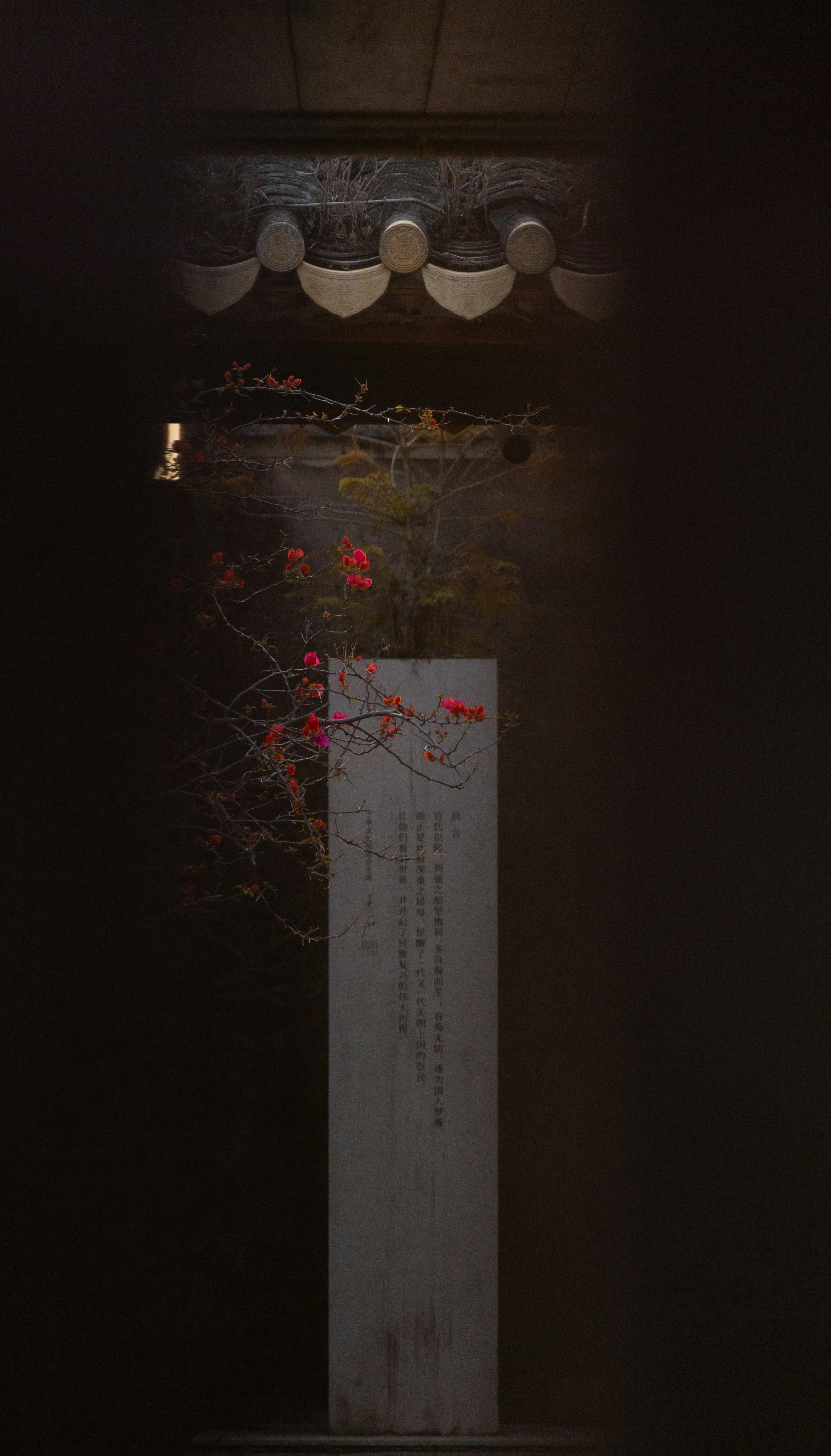 A stone monument with blooming branches in a dark setting.