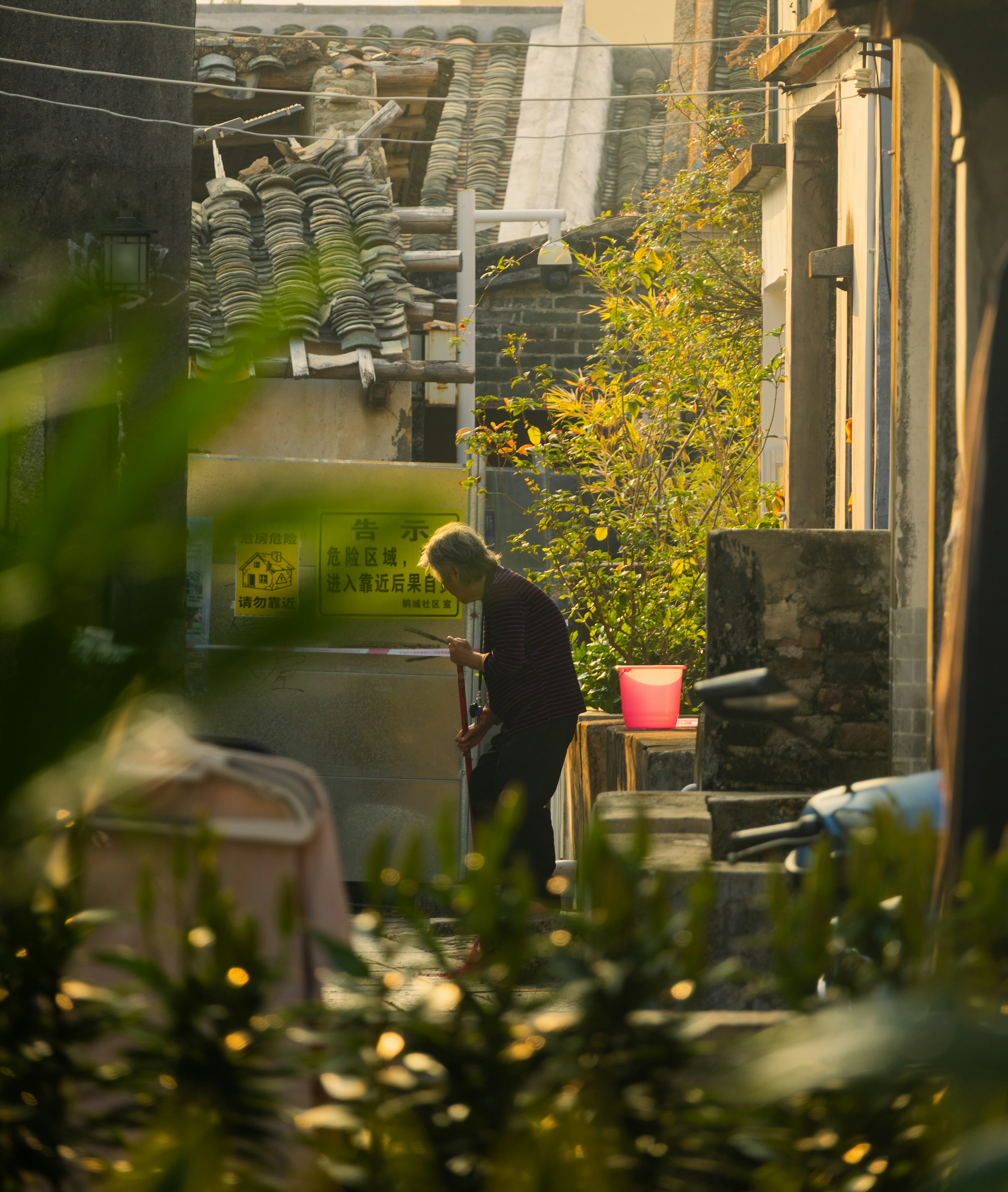 Person sweeping a narrow alleyway at sunset.