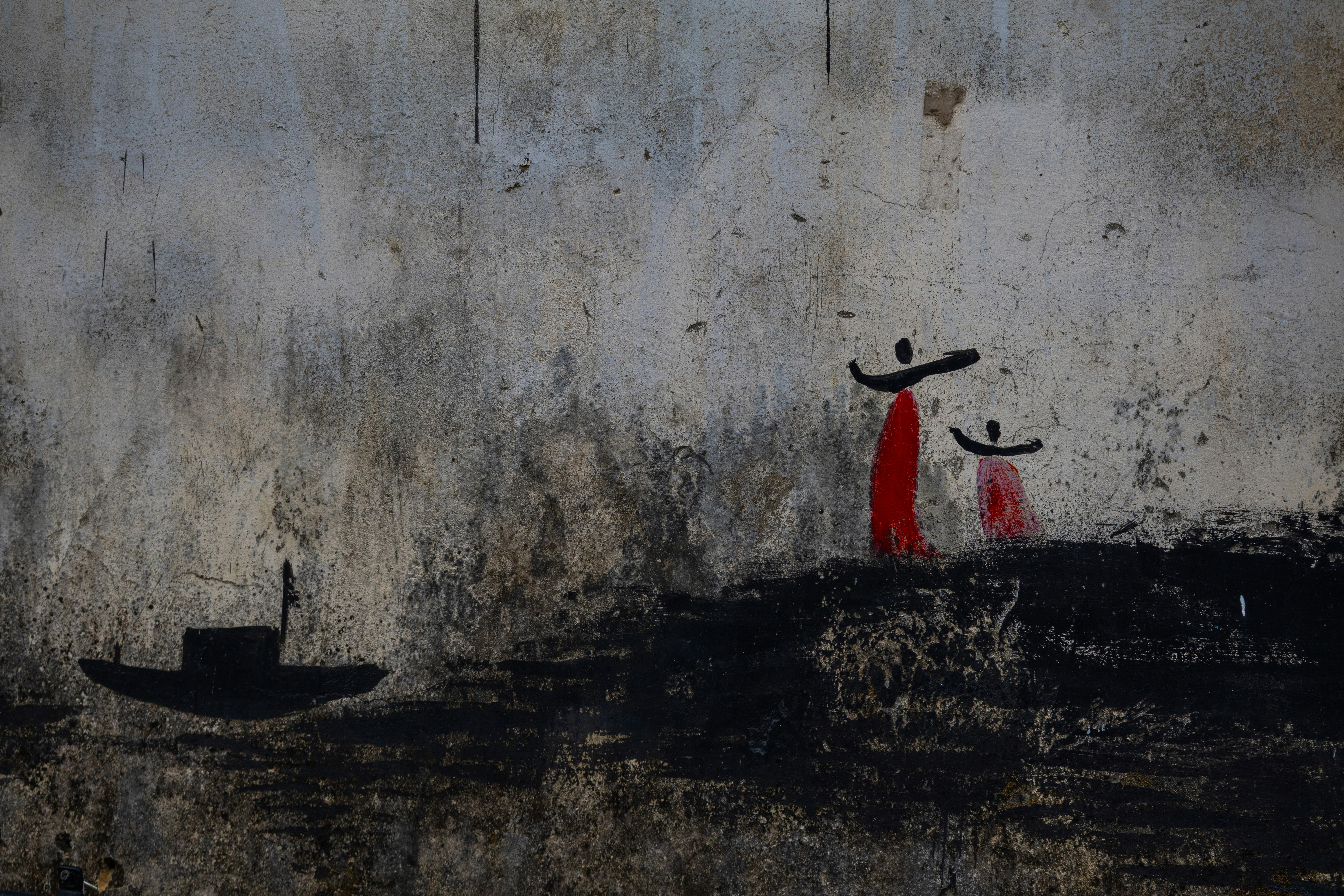 Two figures in red stand near a boat.