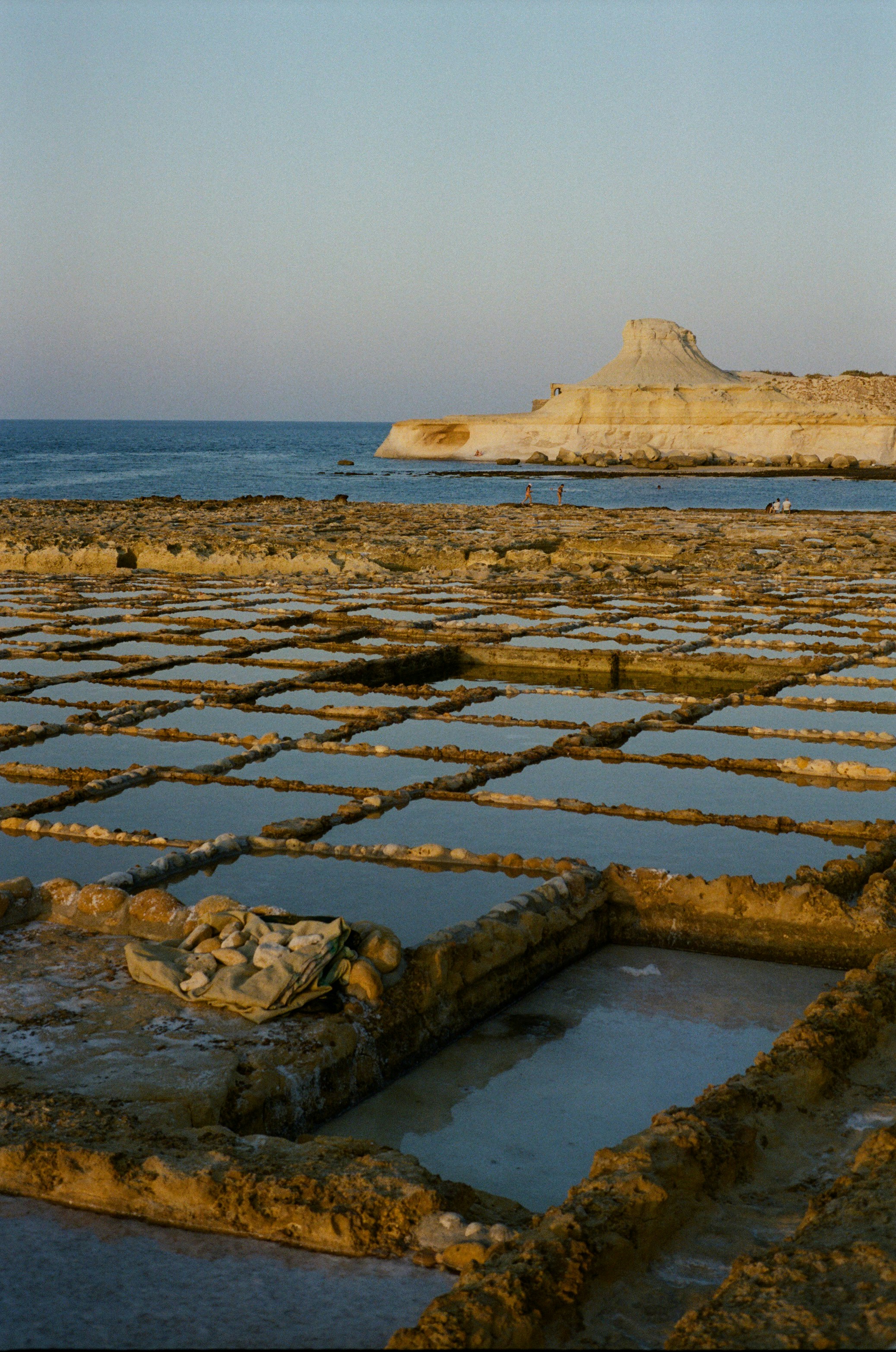 Salt pans by the ocean with distant rocky hills.