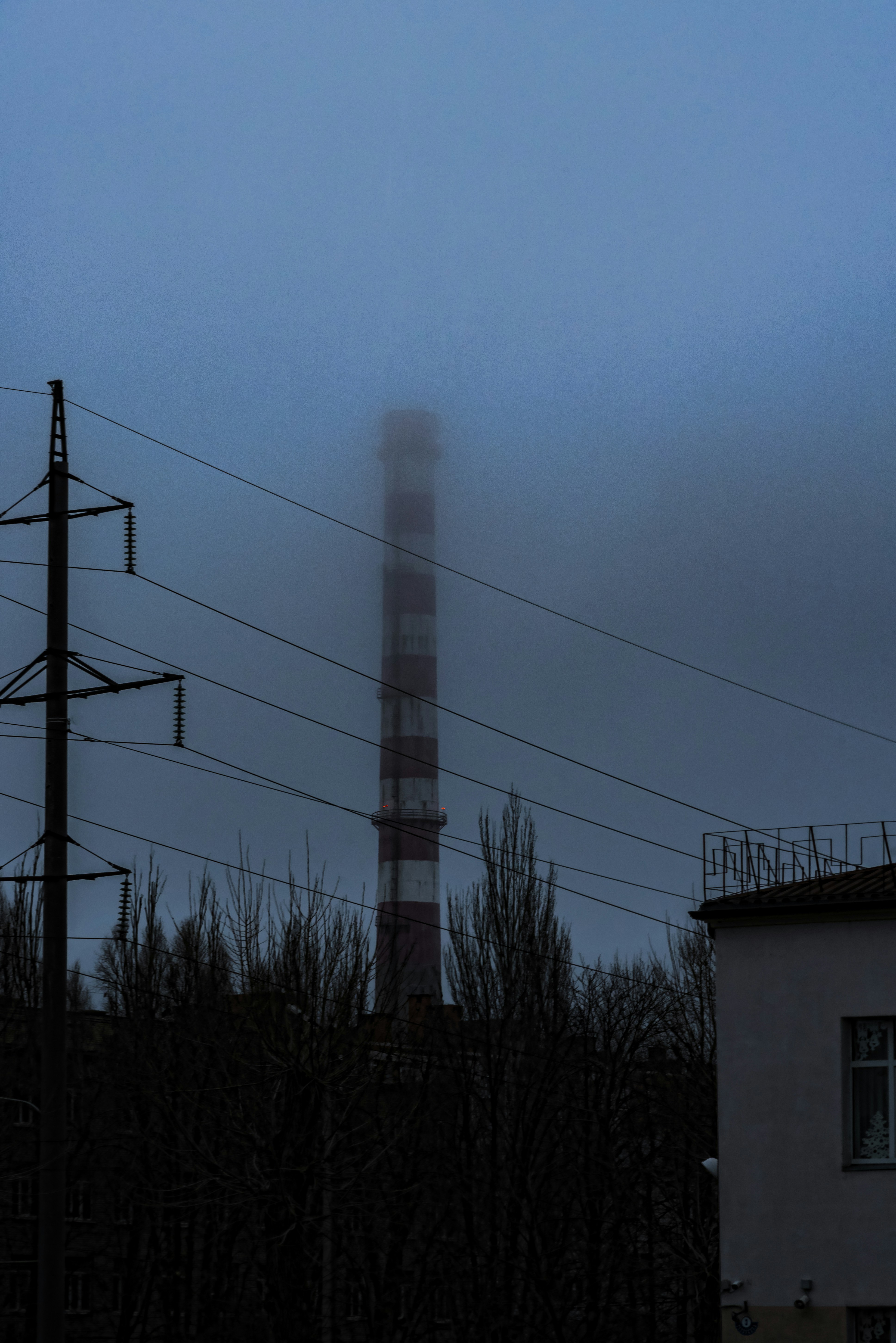 Industrial chimney shrouded in fog with power lines