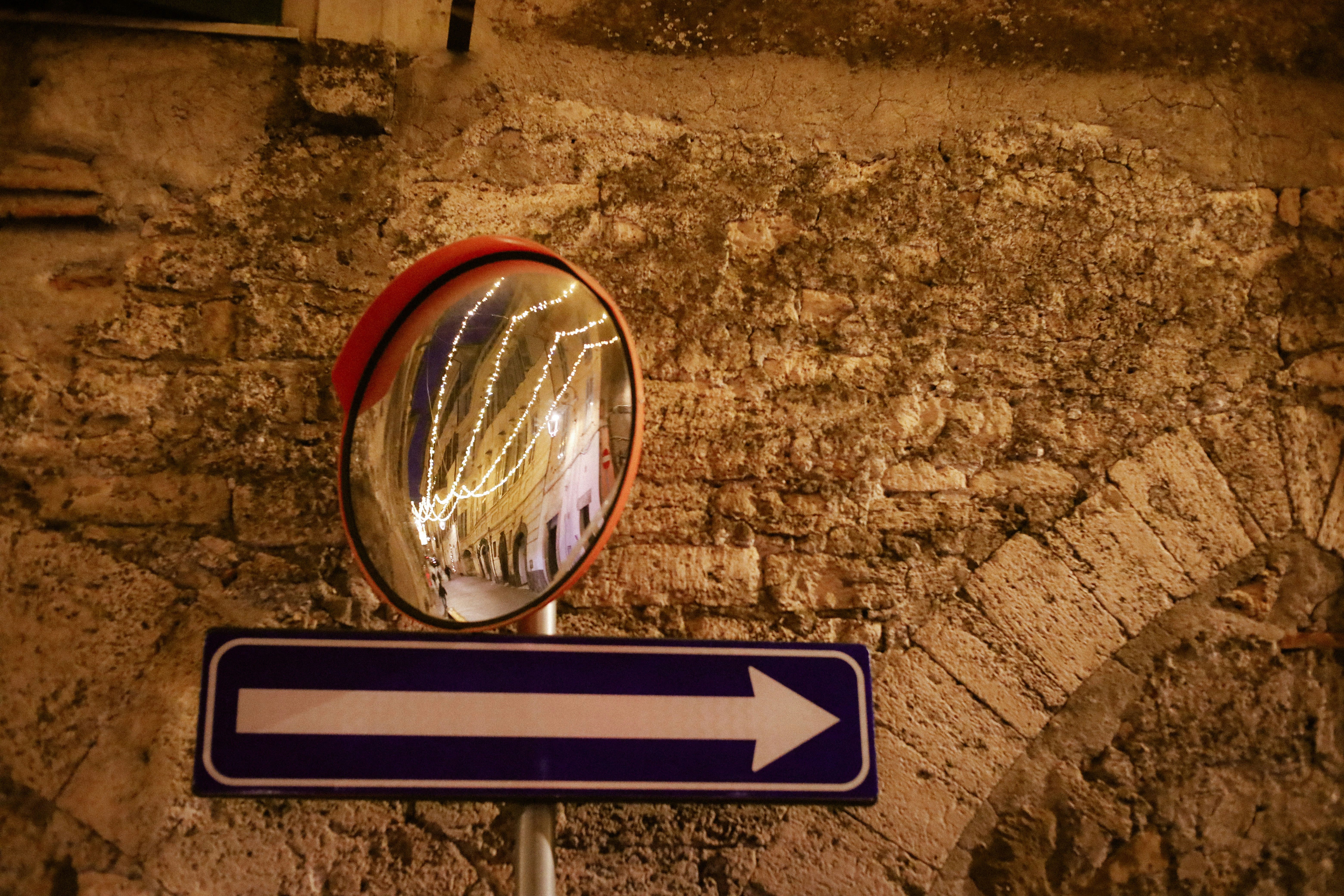 Convex mirror reflects street lights above arrow sign.