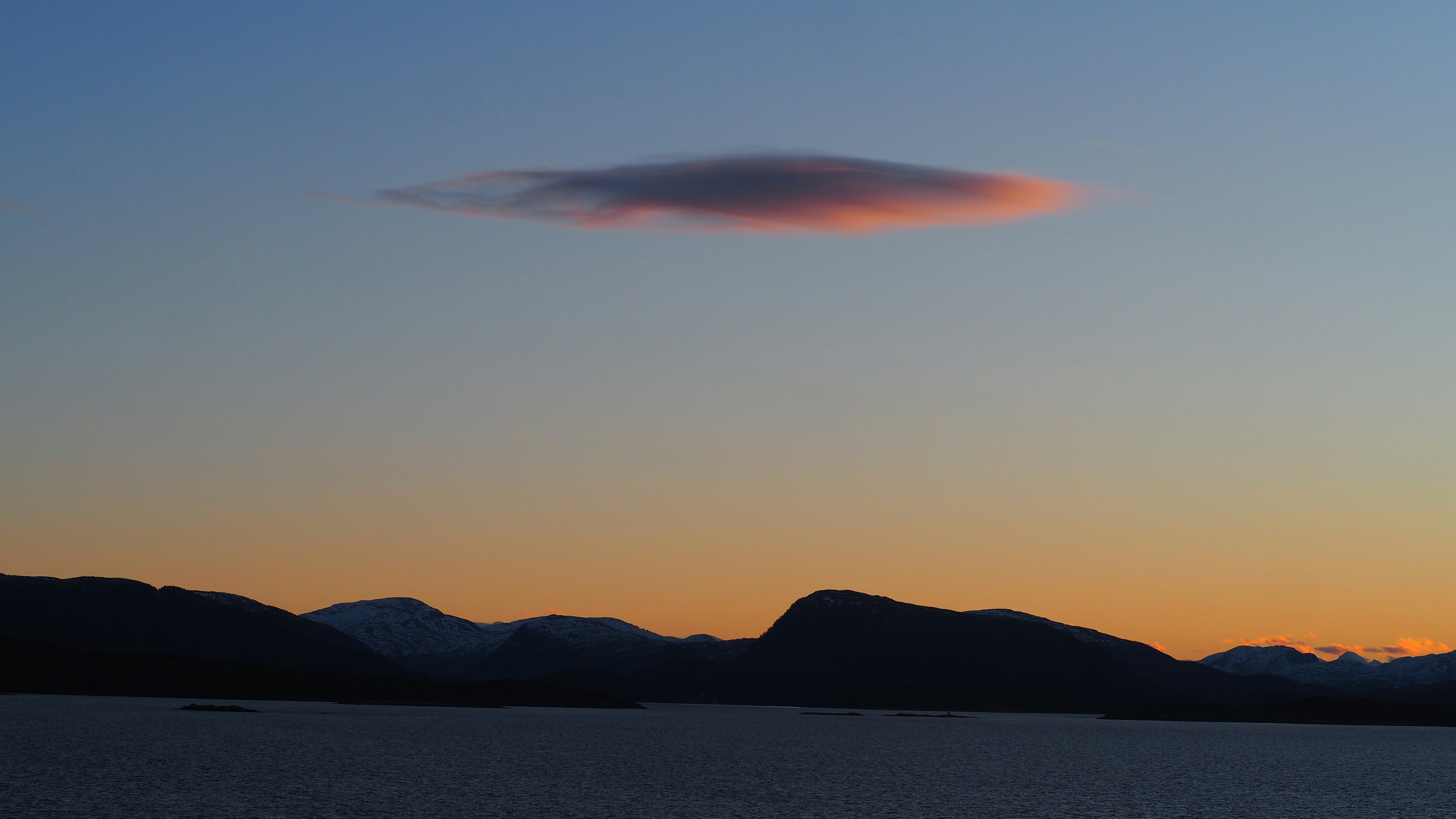 Single lenticular cloud glows at sunset over mountains.